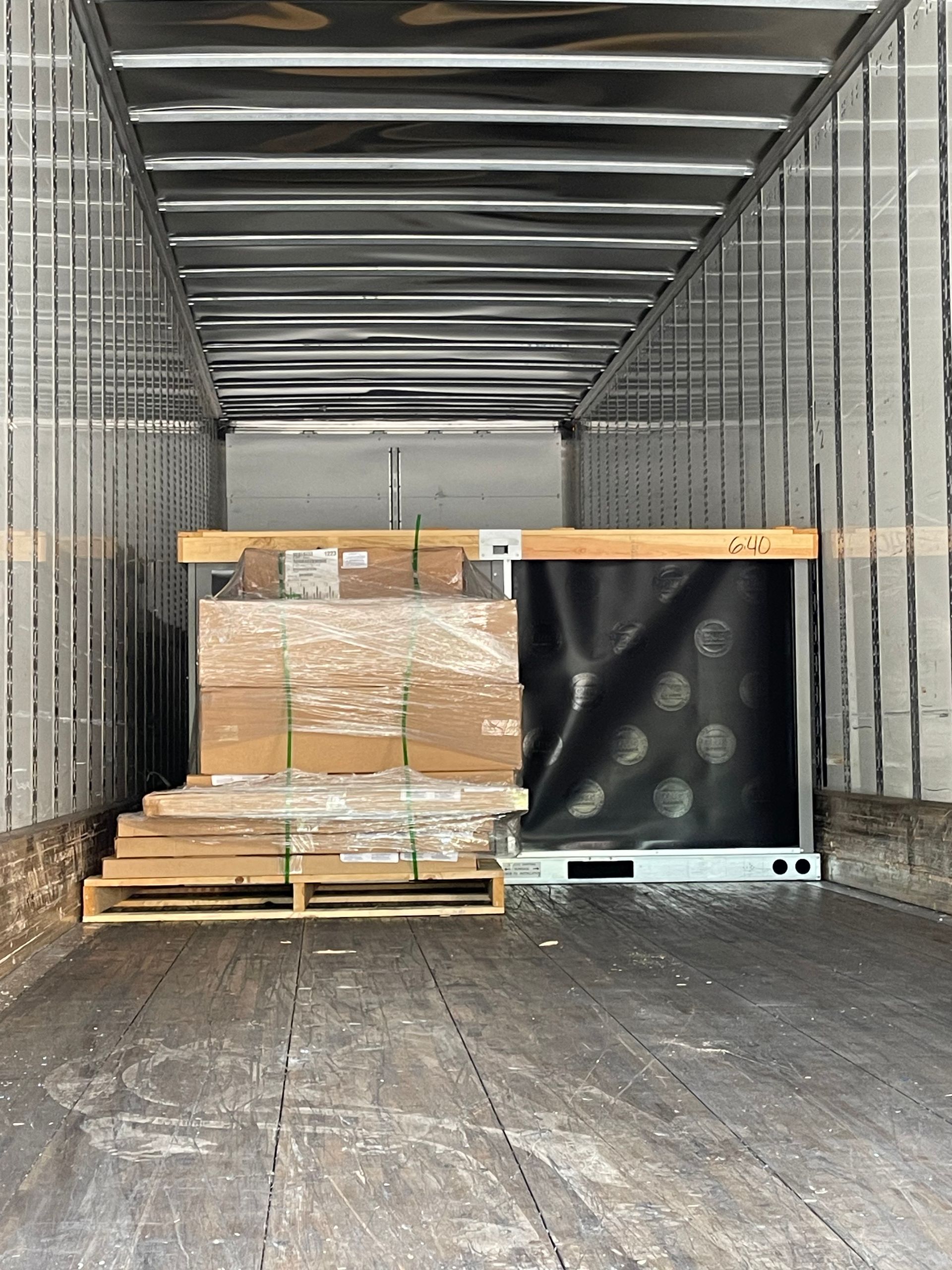 Inside of a truck cargo hold containing stacked cardboard boxes and a pallet.