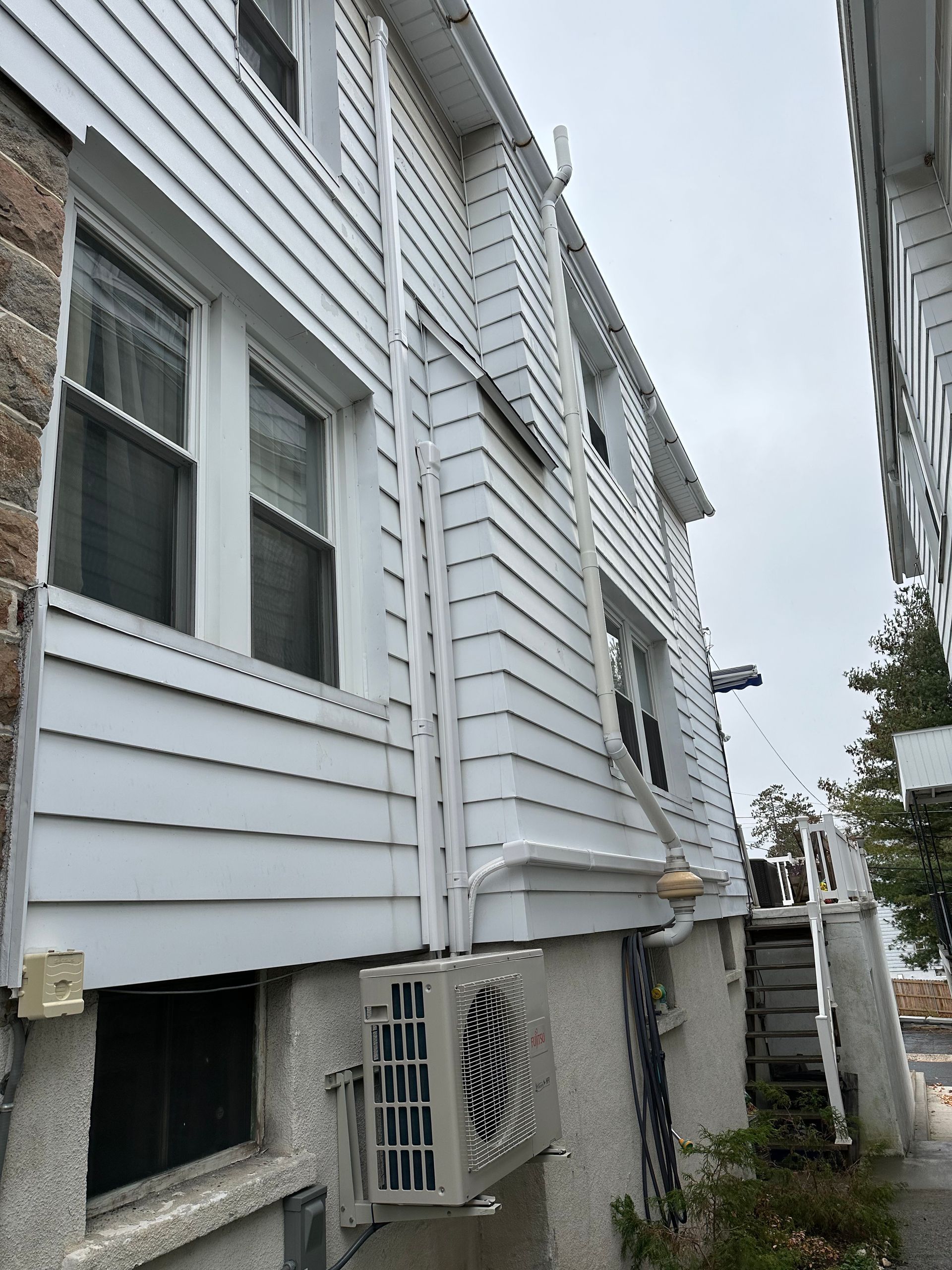 Side view of a white two-story building with an air conditioner unit and a stone wall on the left.