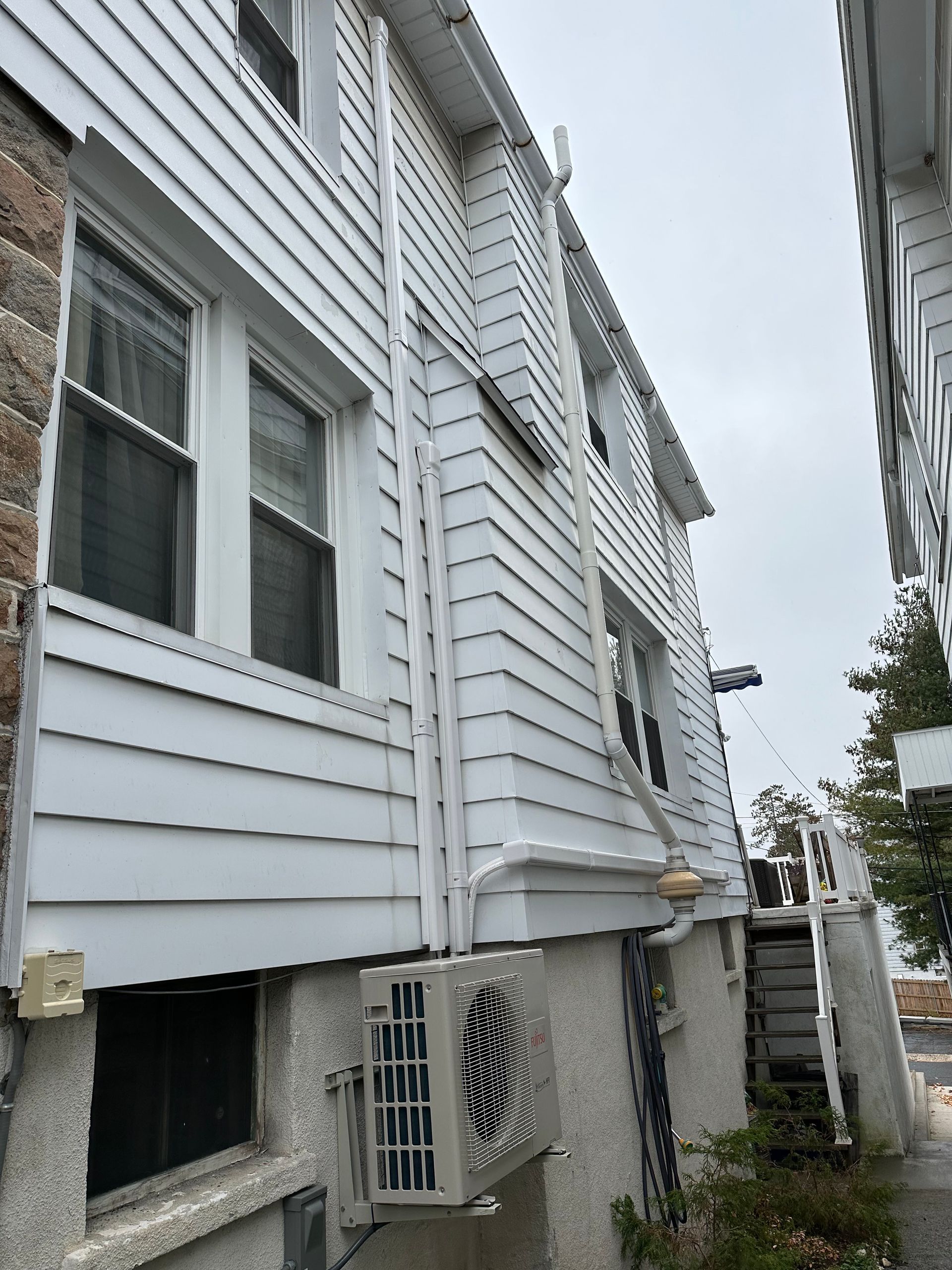 White-sided building with air conditioning unit, windows, and a narrow alleyway.