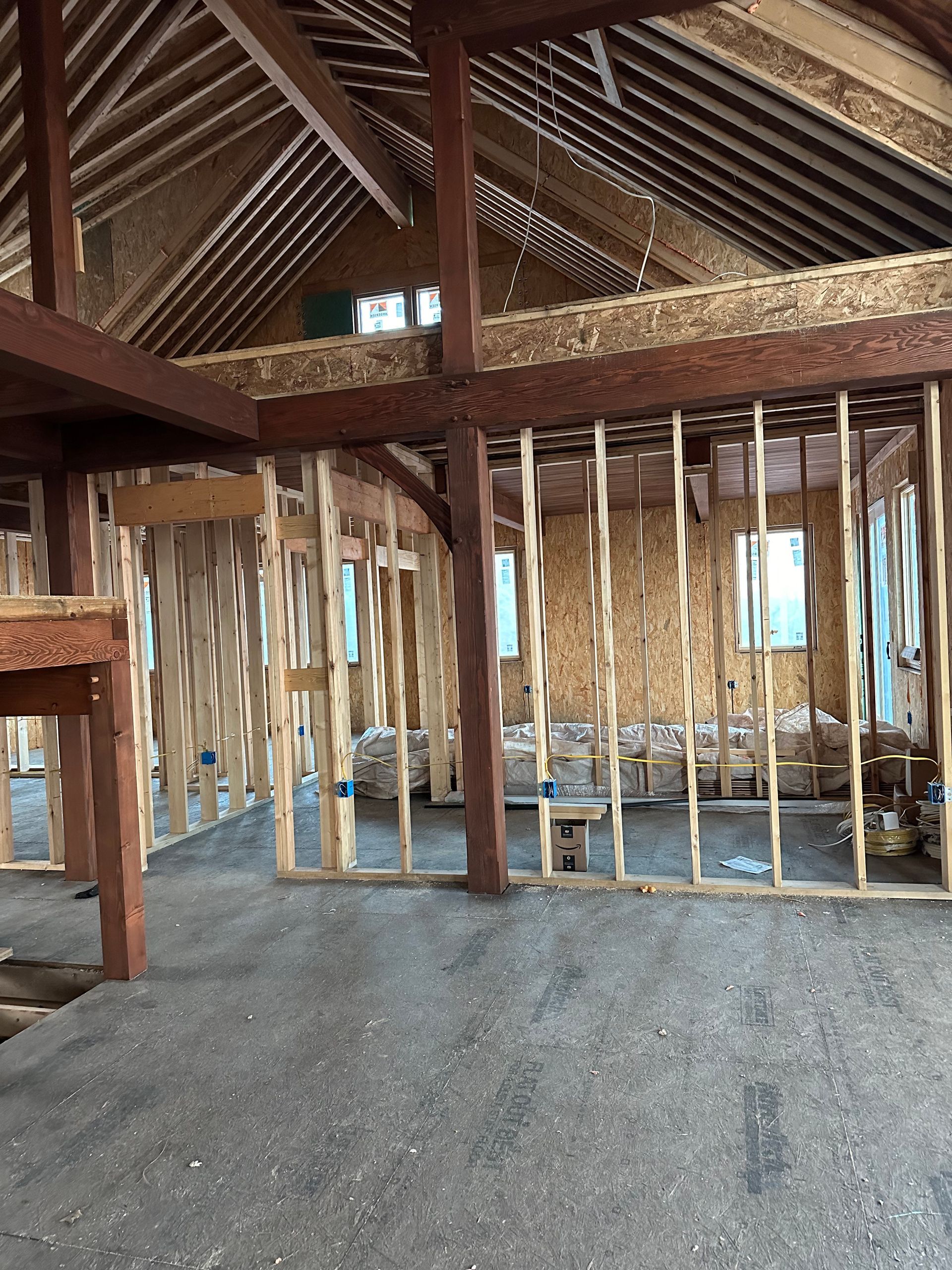 Interior view of a building under construction, showing exposed wooden framing, beams, and a loft area.
