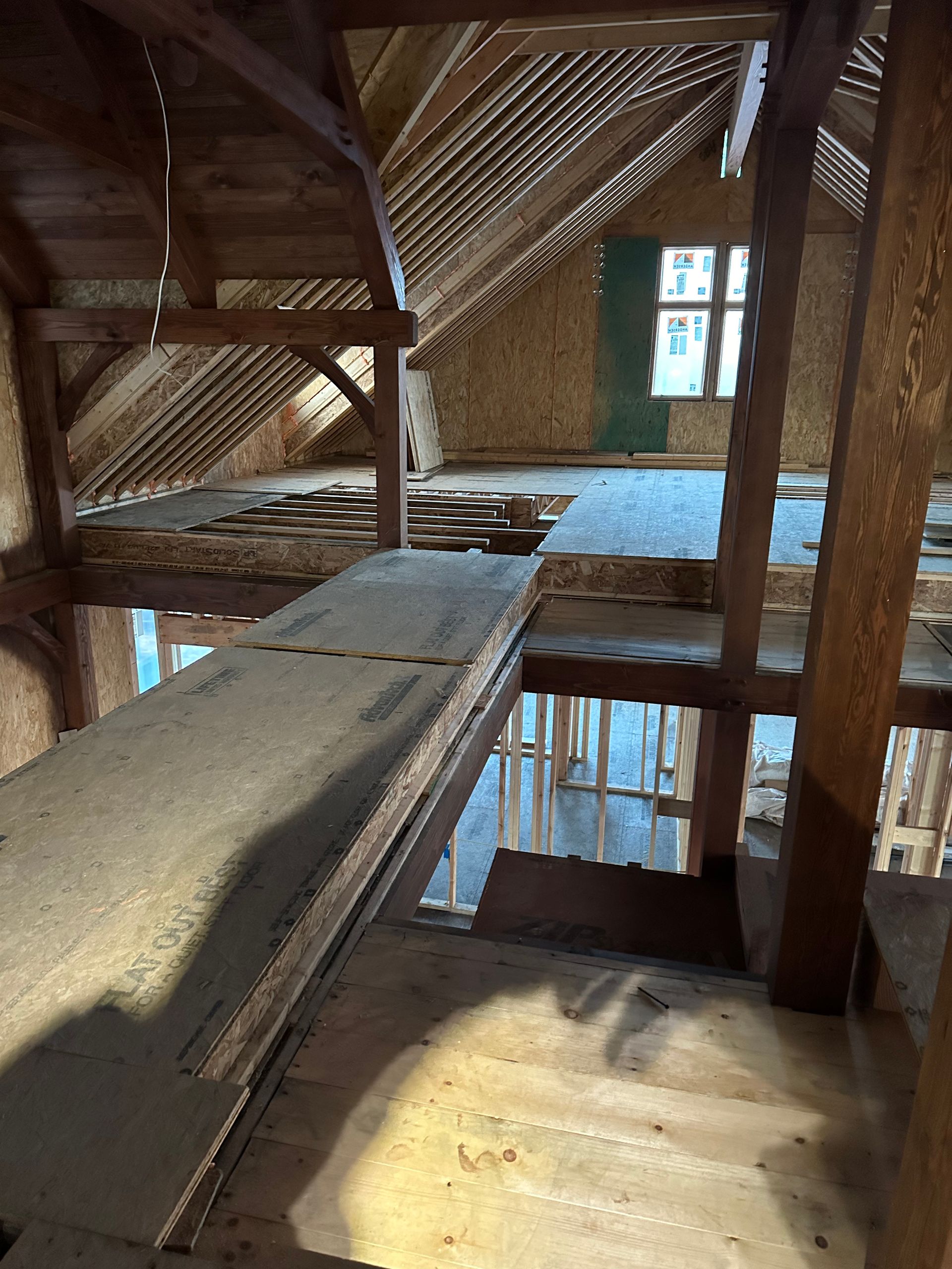 Interior of an unfinished attic with wooden beams, exposed rafters, and a bridge-like walkway.
