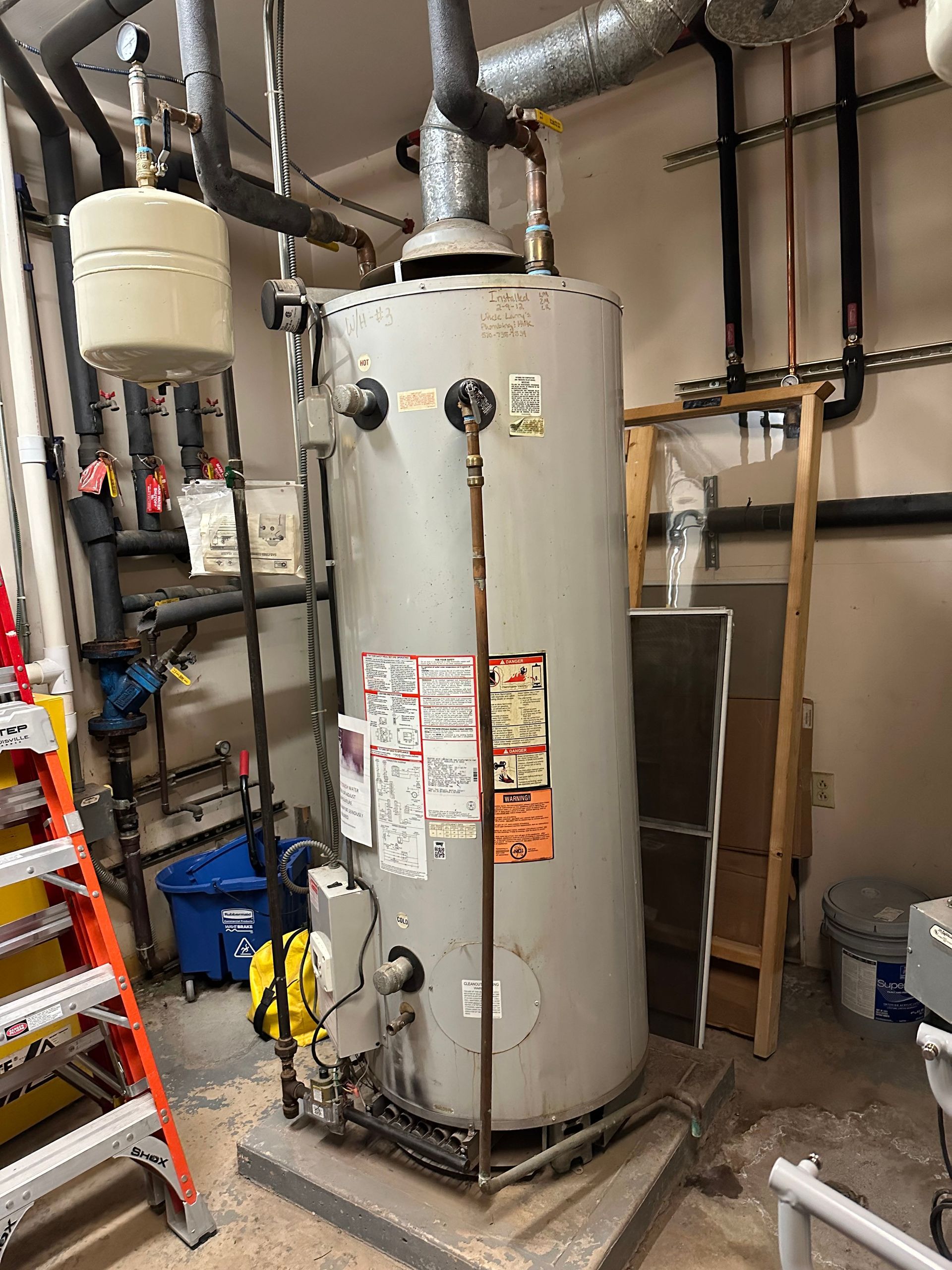Water heater in a utility room, with pipes and other equipment.