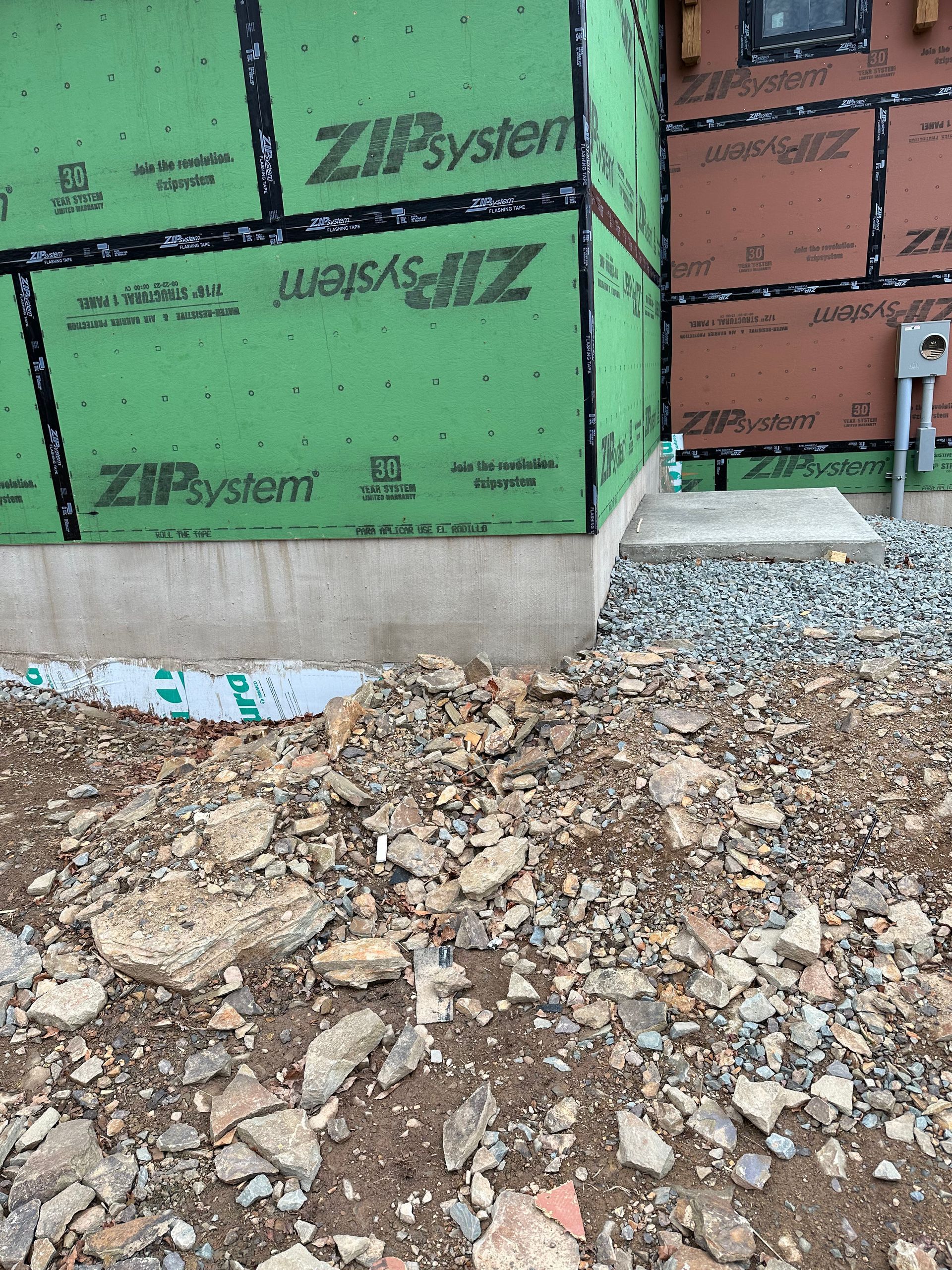 Green Zip System siding on a new building, with a concrete foundation and gravel pathway under construction.
