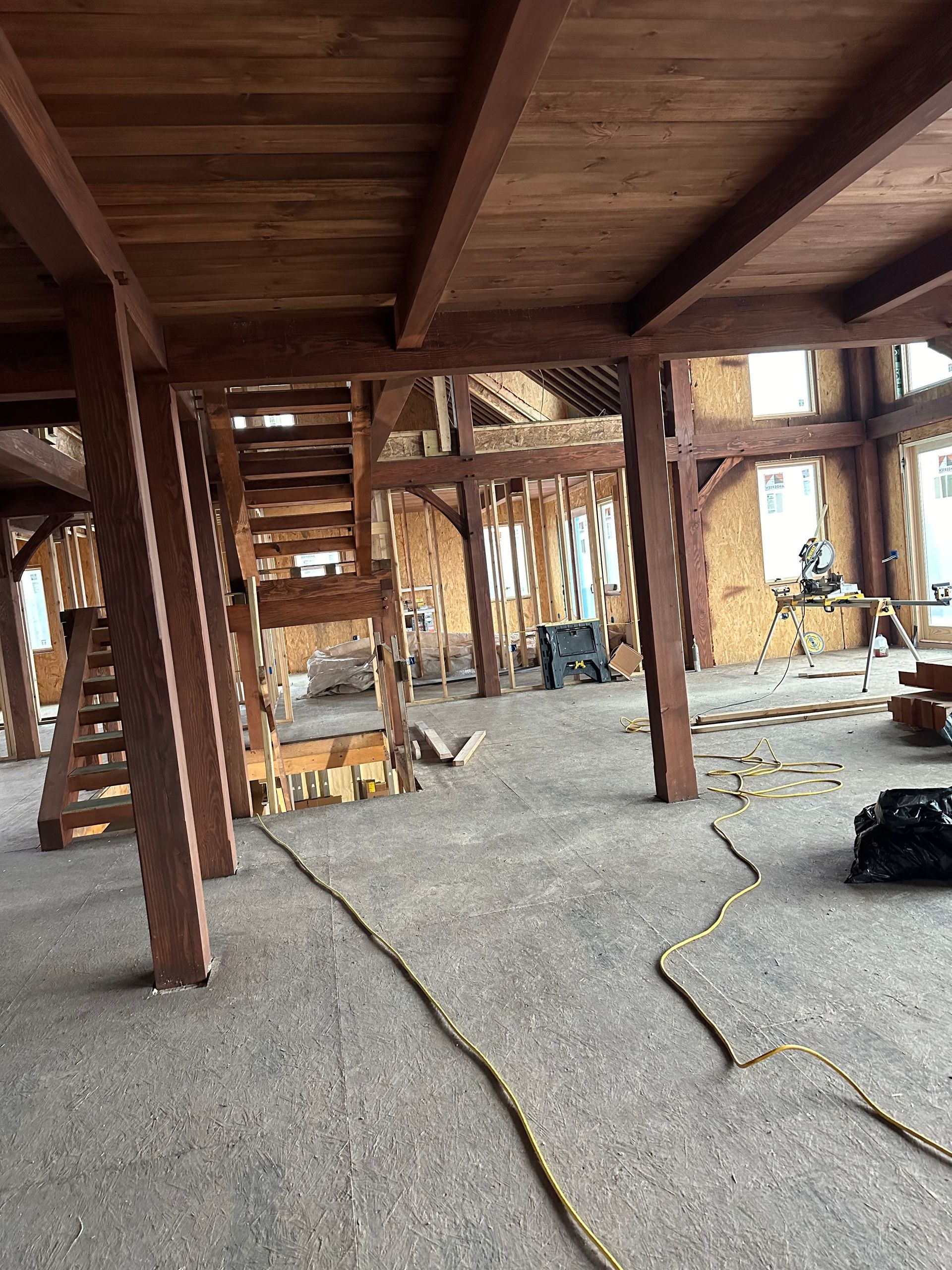 Interior of a building under construction with exposed wood beams, stairs, and concrete floor.