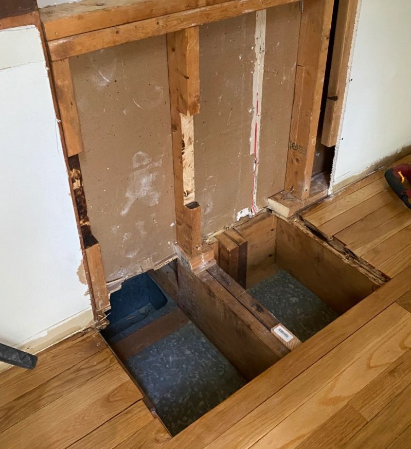 Framed wall opening revealing unfinished construction, dark flooring around opening.