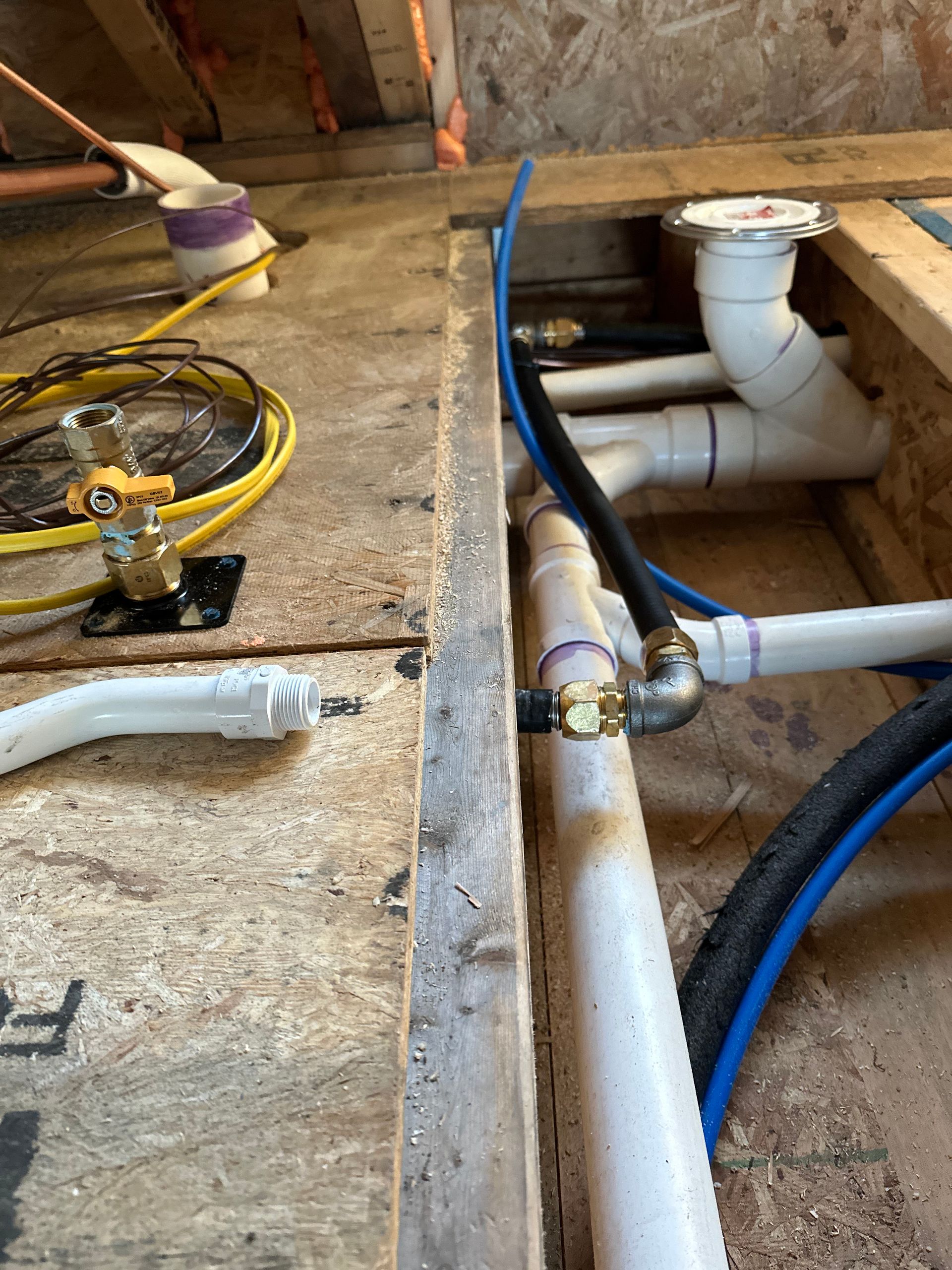 Plumbing pipes under construction in a wooden floor, including white PVC and blue PEX.