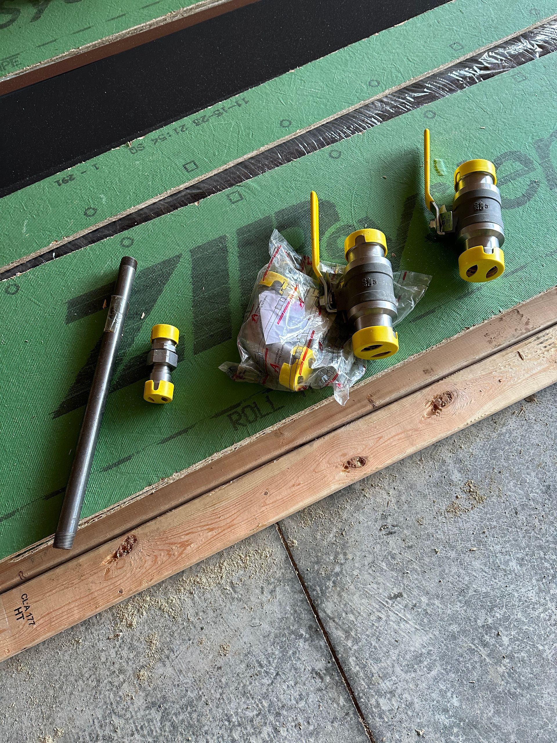 Gas valve components on green sheathing and wood; yellow valves and metal pipe.