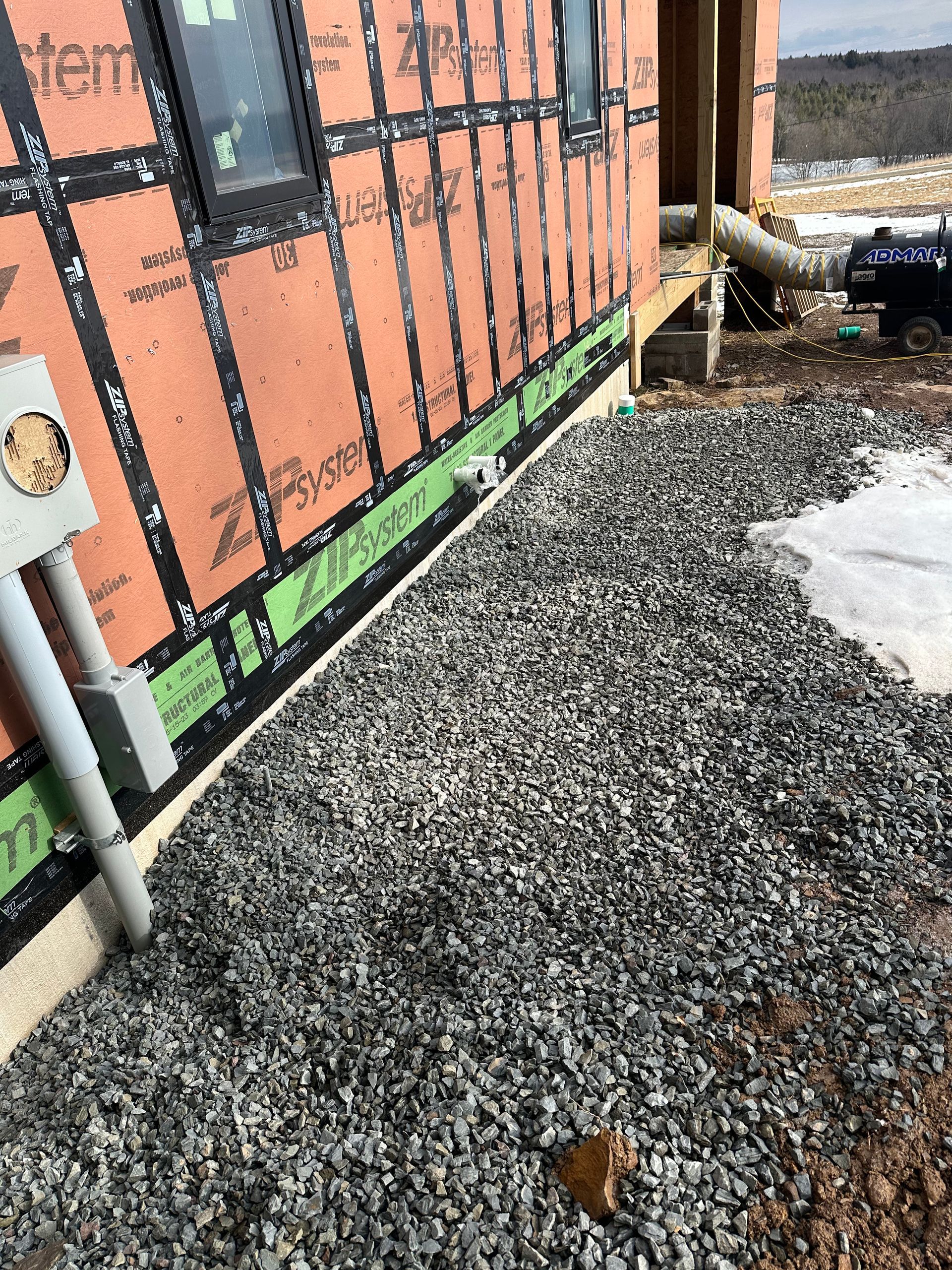 Exterior wall with gravel bed, electrical box, black wrap, and green flashing.