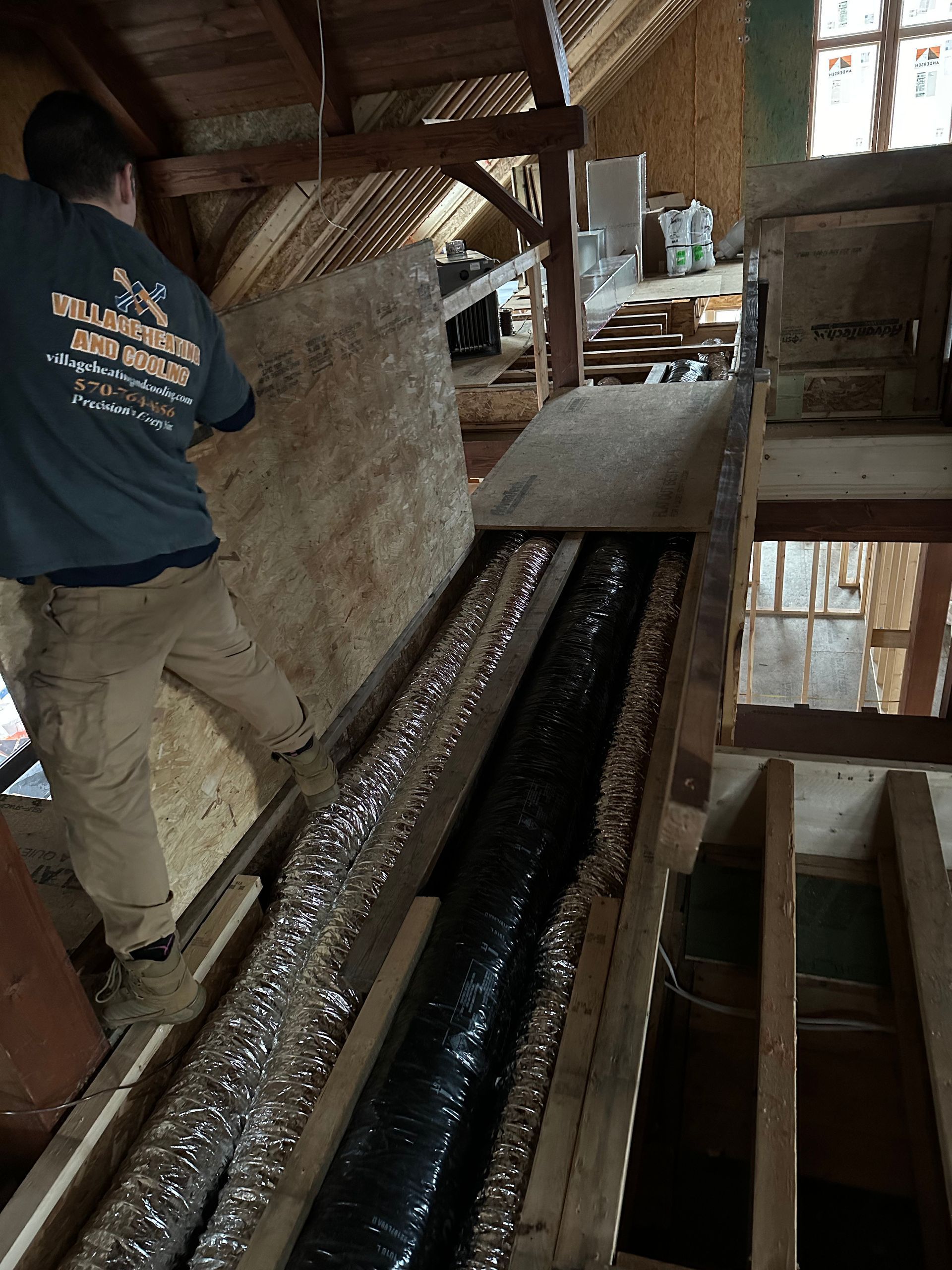 Person installing insulation in an attic; the area is under construction with exposed beams and a long duct.