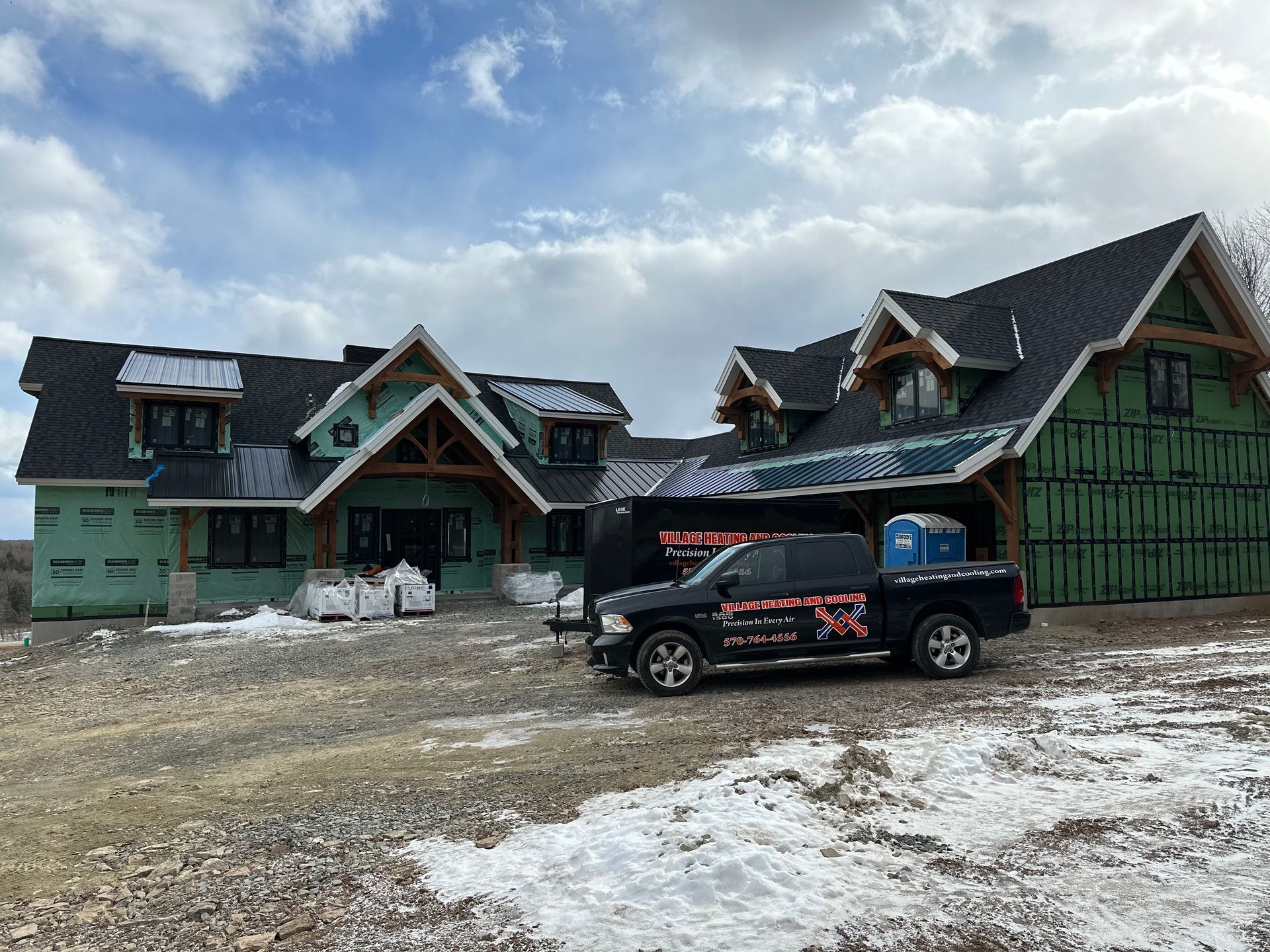 Construction site: House under construction, black truck, snowy ground, blue sky.