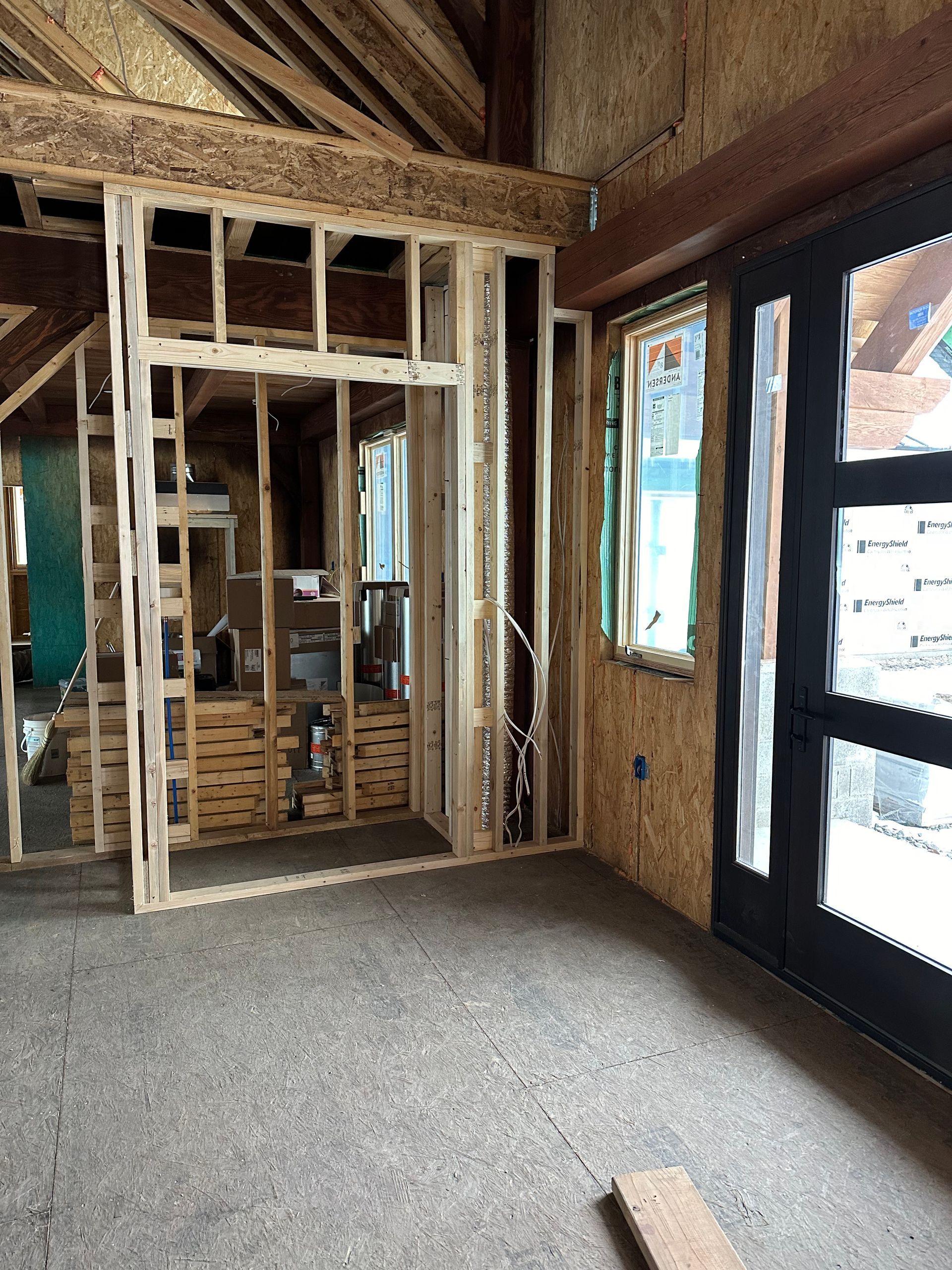 Interior construction: wooden framing for a wall, door, and window in a room with concrete floor.