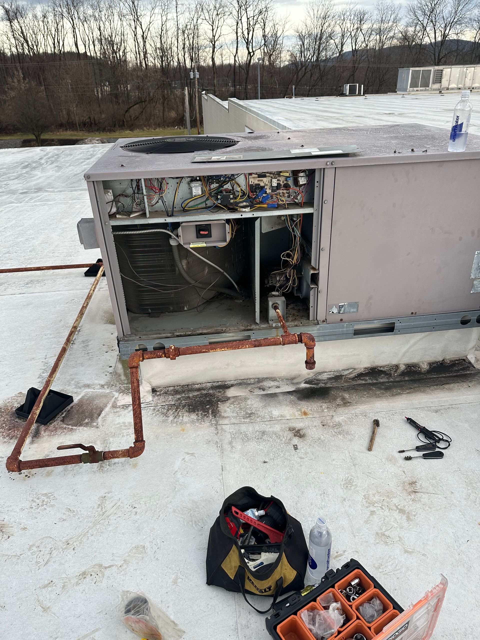 HVAC unit on a rooftop, open for repair. Copper pipes and tools lie nearby.