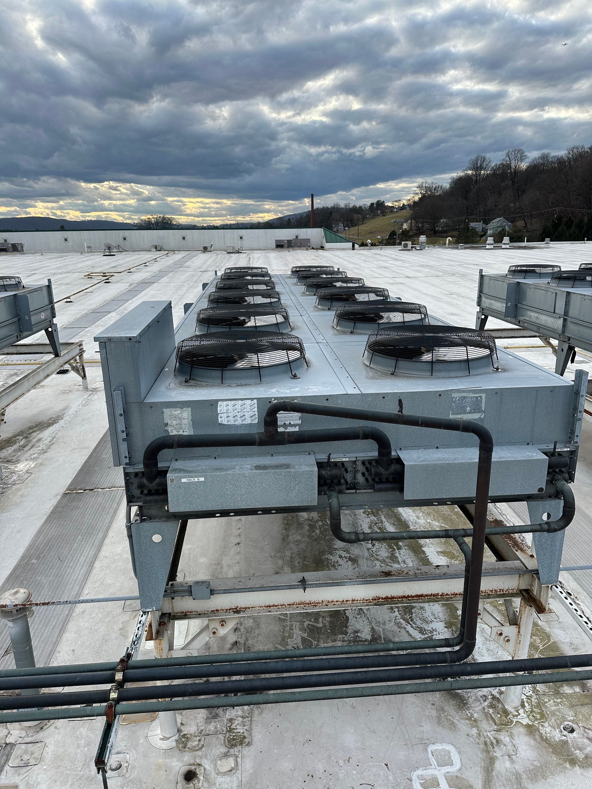 Rooftop HVAC unit with multiple fans against a cloudy sky.