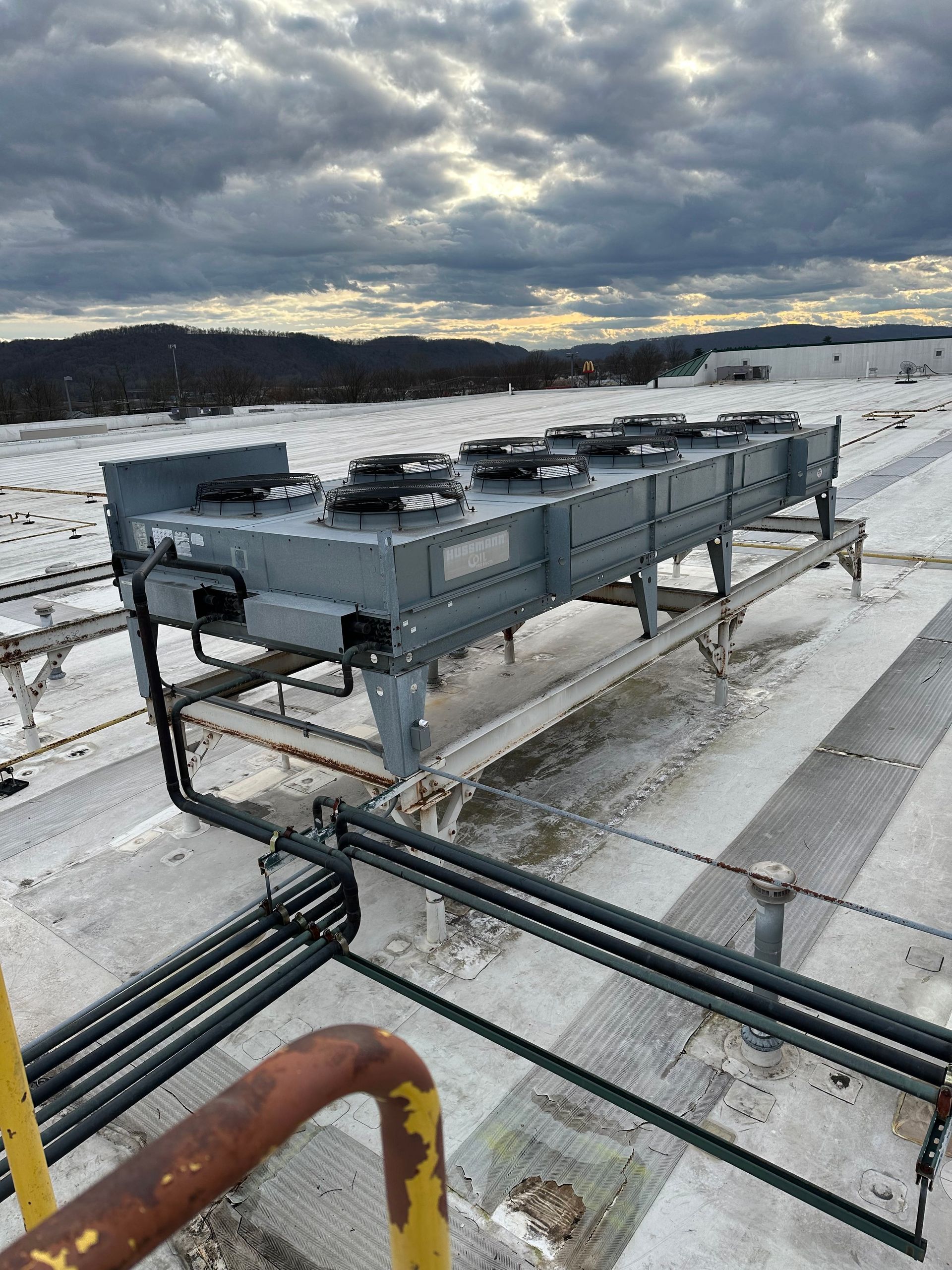 Rooftop HVAC unit with multiple fans against a cloudy sky.