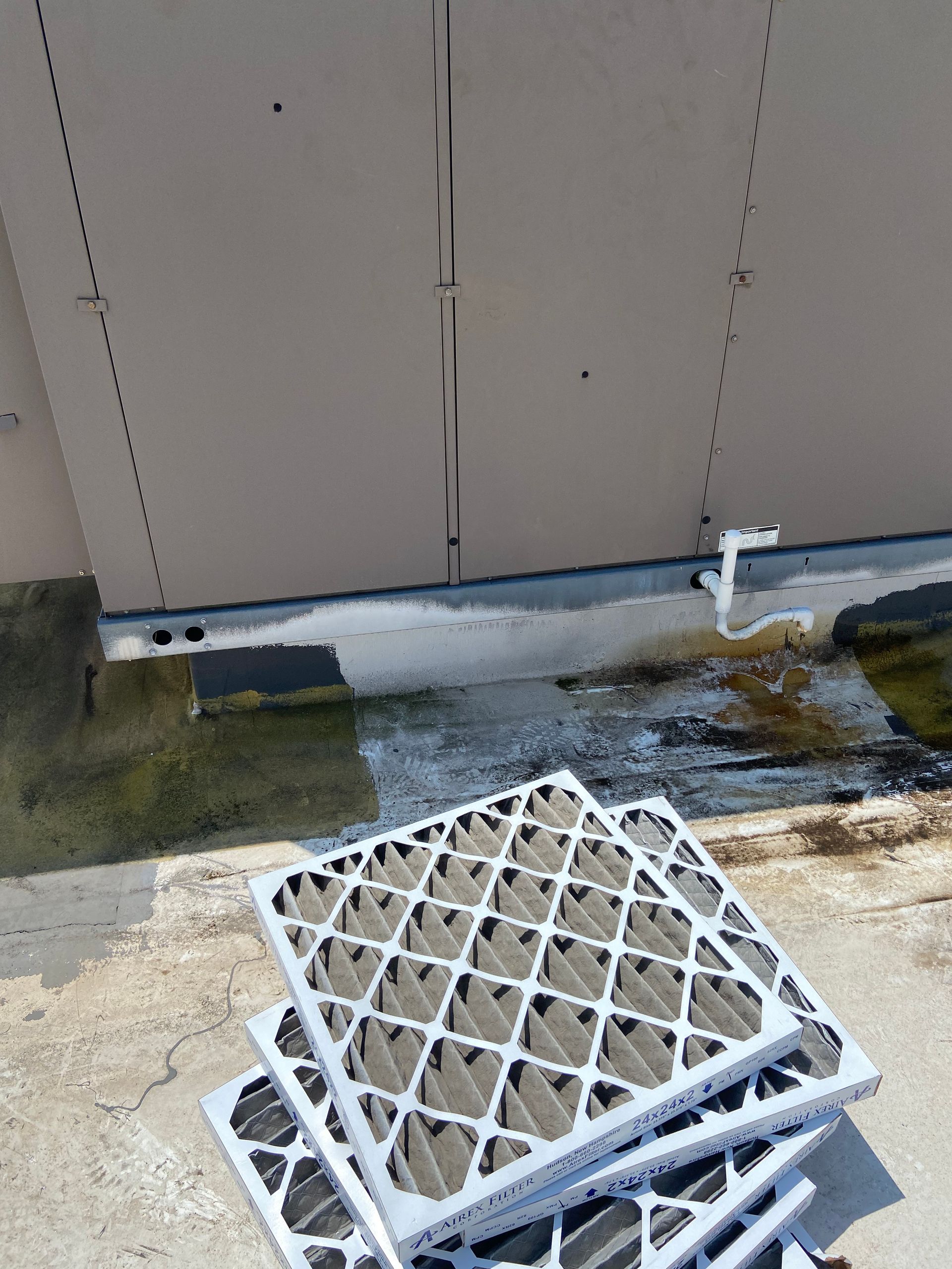 Stack of dirty air filters on a rooftop, next to a weathered building with water stains.