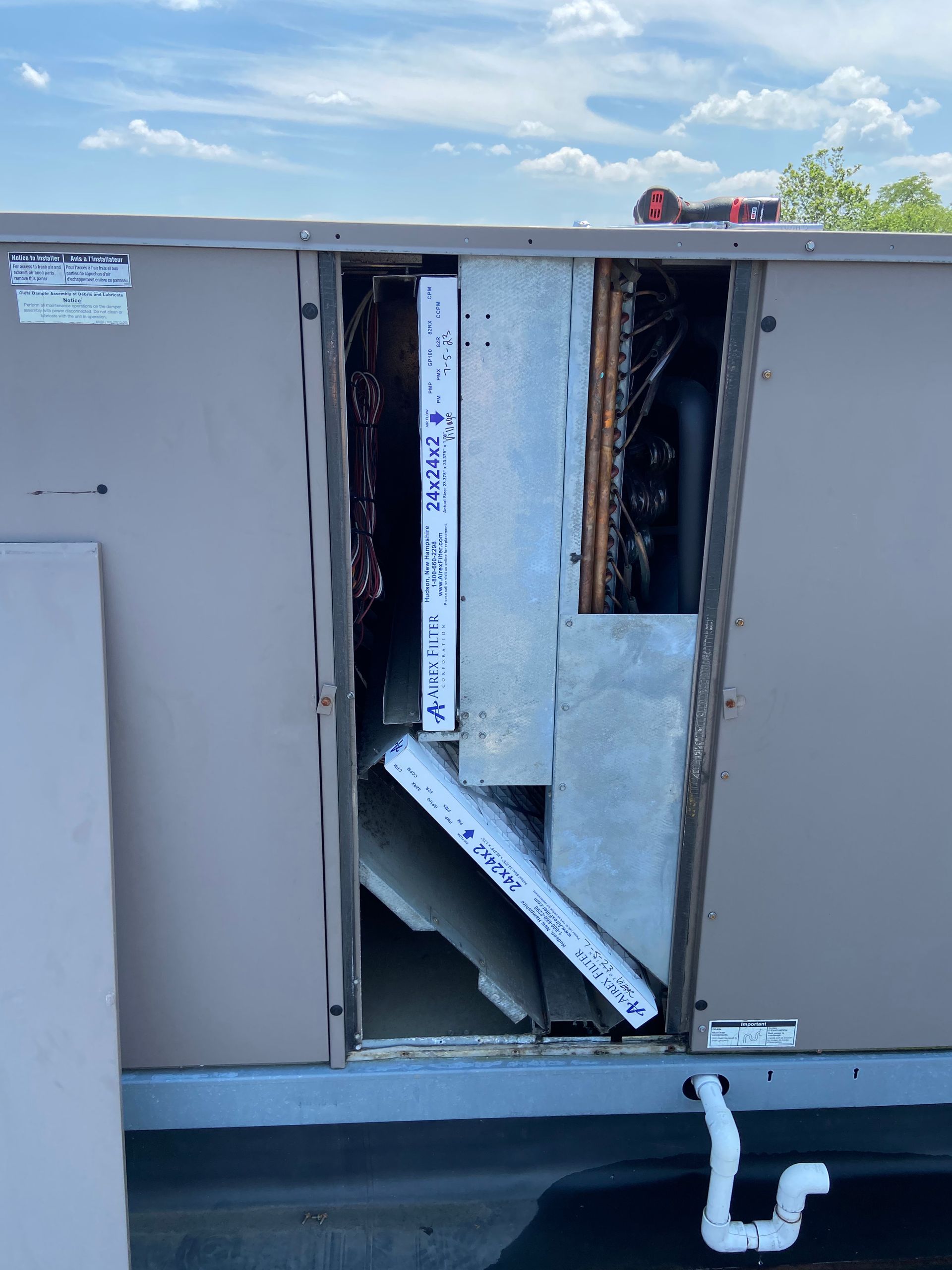 HVAC unit with a panel removed, showing internal components. Rooftop setting, cloudy sky.