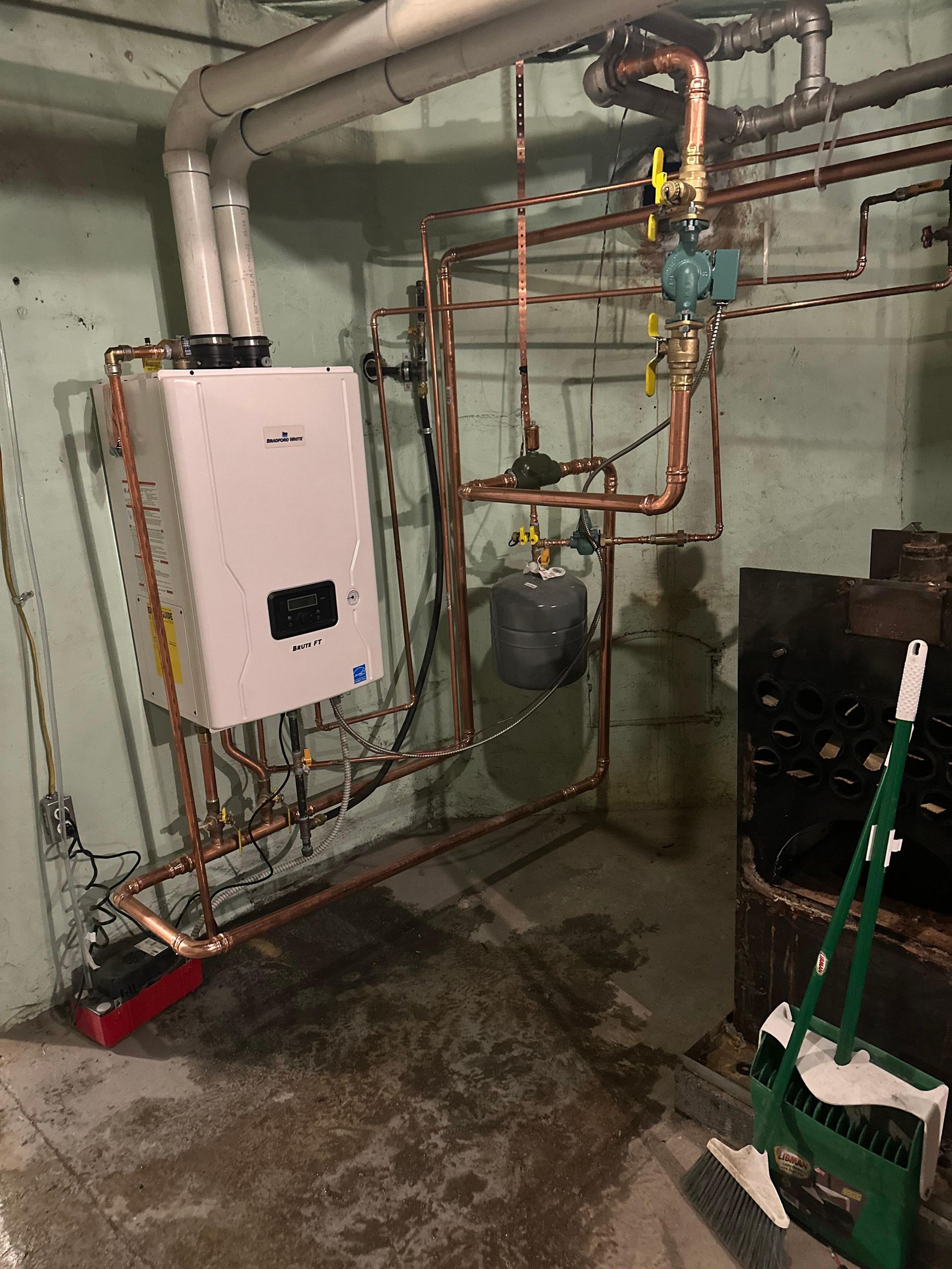 A modern gas boiler and related copper piping in a basement setting. Various valves and a small pressure tank visible.