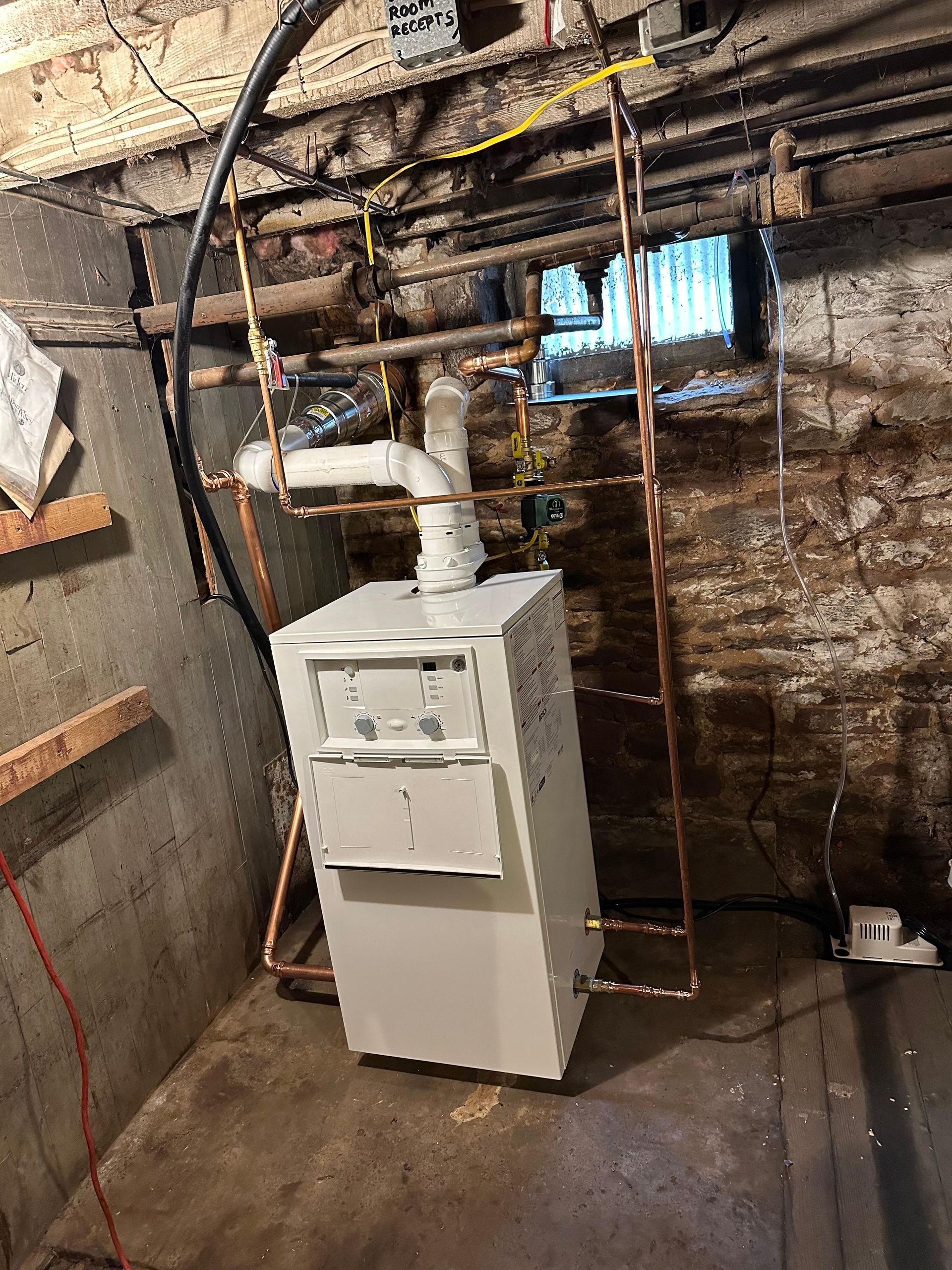 Furnace in a basement with copper pipes and exposed brick walls.