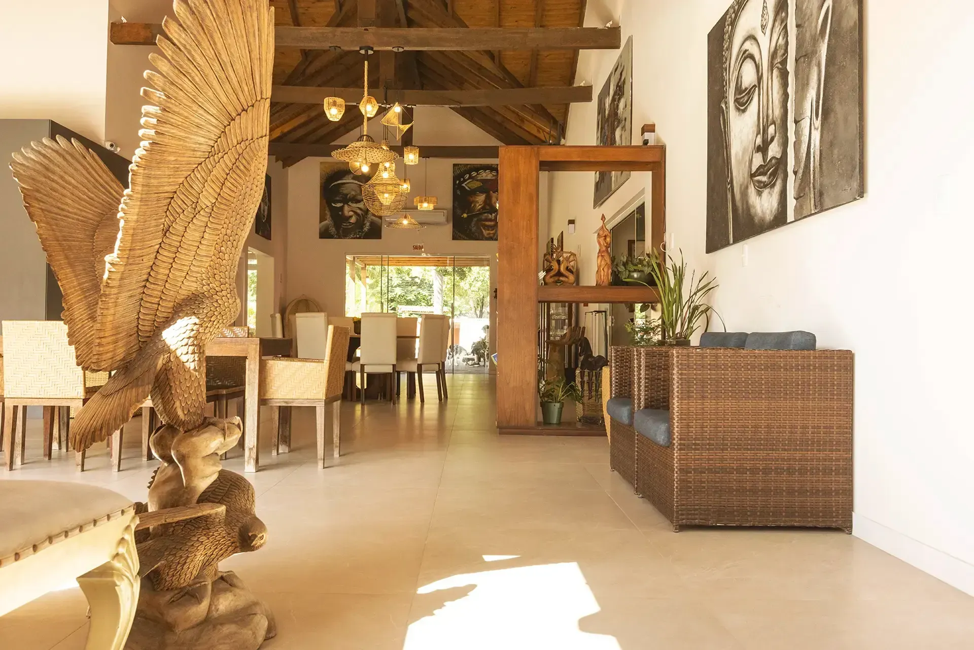 Interior espaçoso com esculturas de madeira, área de jantar, obras de arte de Buda e móveis de vime.