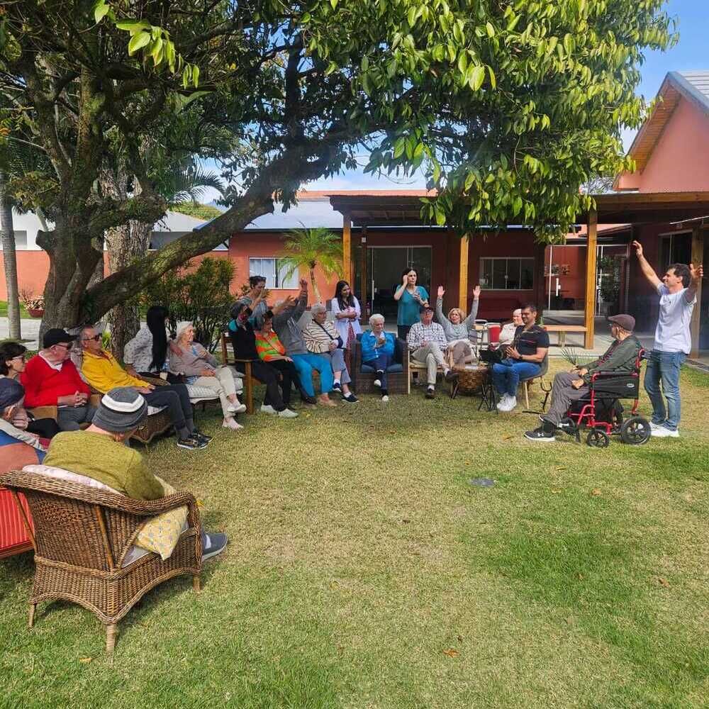 Pessoas idosas em um jantar de Natal, usando chapéus de Papai Noel, camisas brancas, ao redor de uma mesa com comida e decorações.