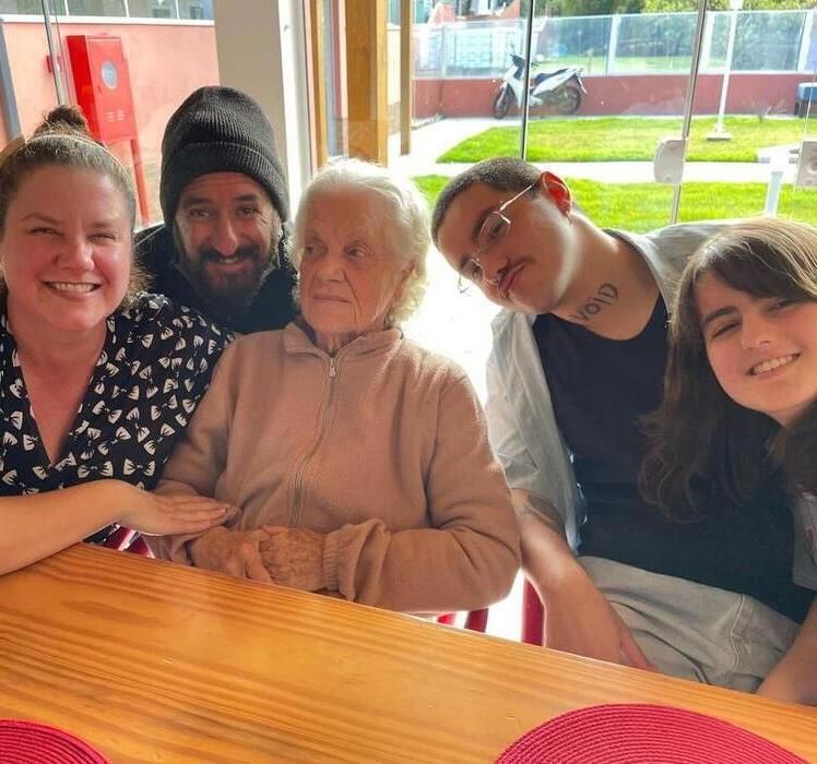 Três pessoas sorrindo juntas: mulher à esquerda vestindo casaco rosa, mulher idosa no centro, Dr. Sergio Tezza à direita vestindo jaqueta branca.