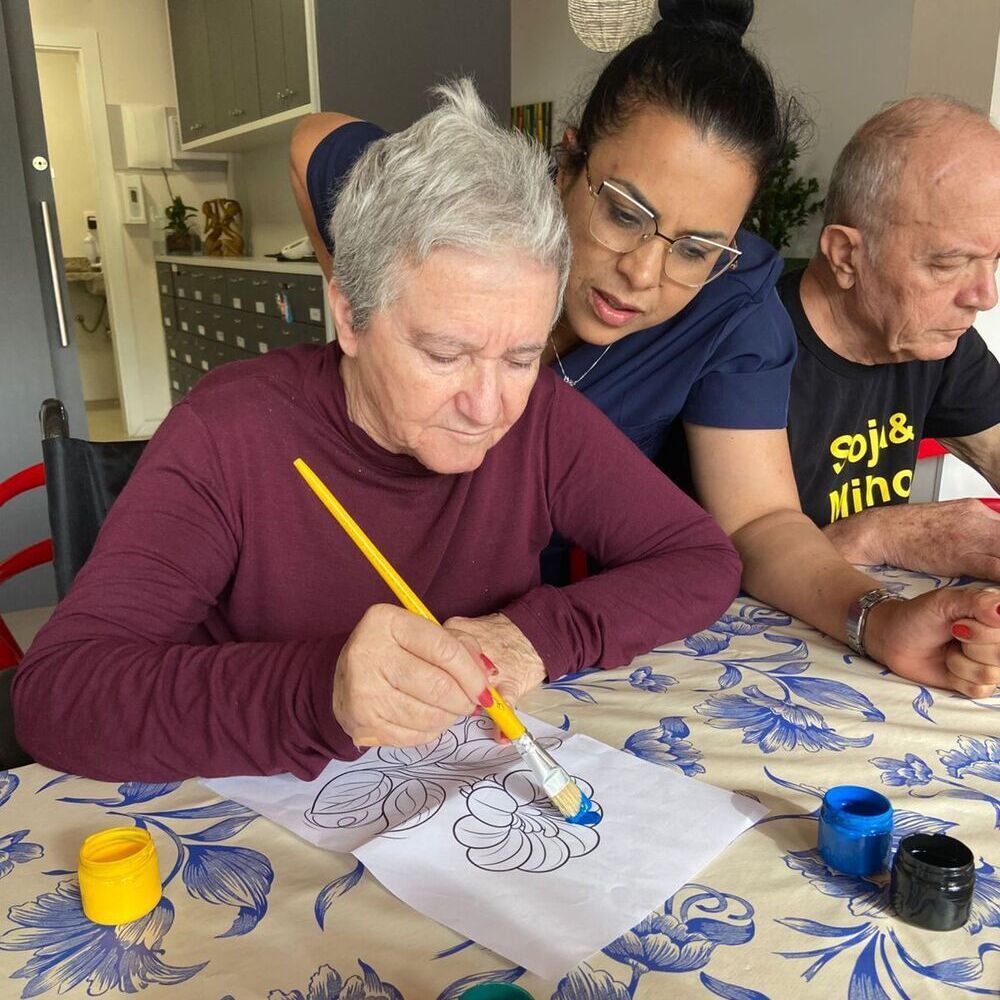 Uma senhora idosa vestida de azul, Dr. Sergio Tezza e uma criança. A criança observa, com balões de aniversário ao fundo.