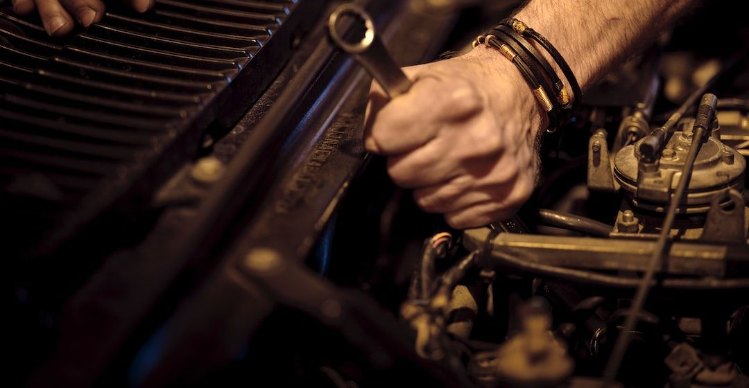 Two men reviewing paperwork near a car on a lift in a garage; a mechanic works below the car.