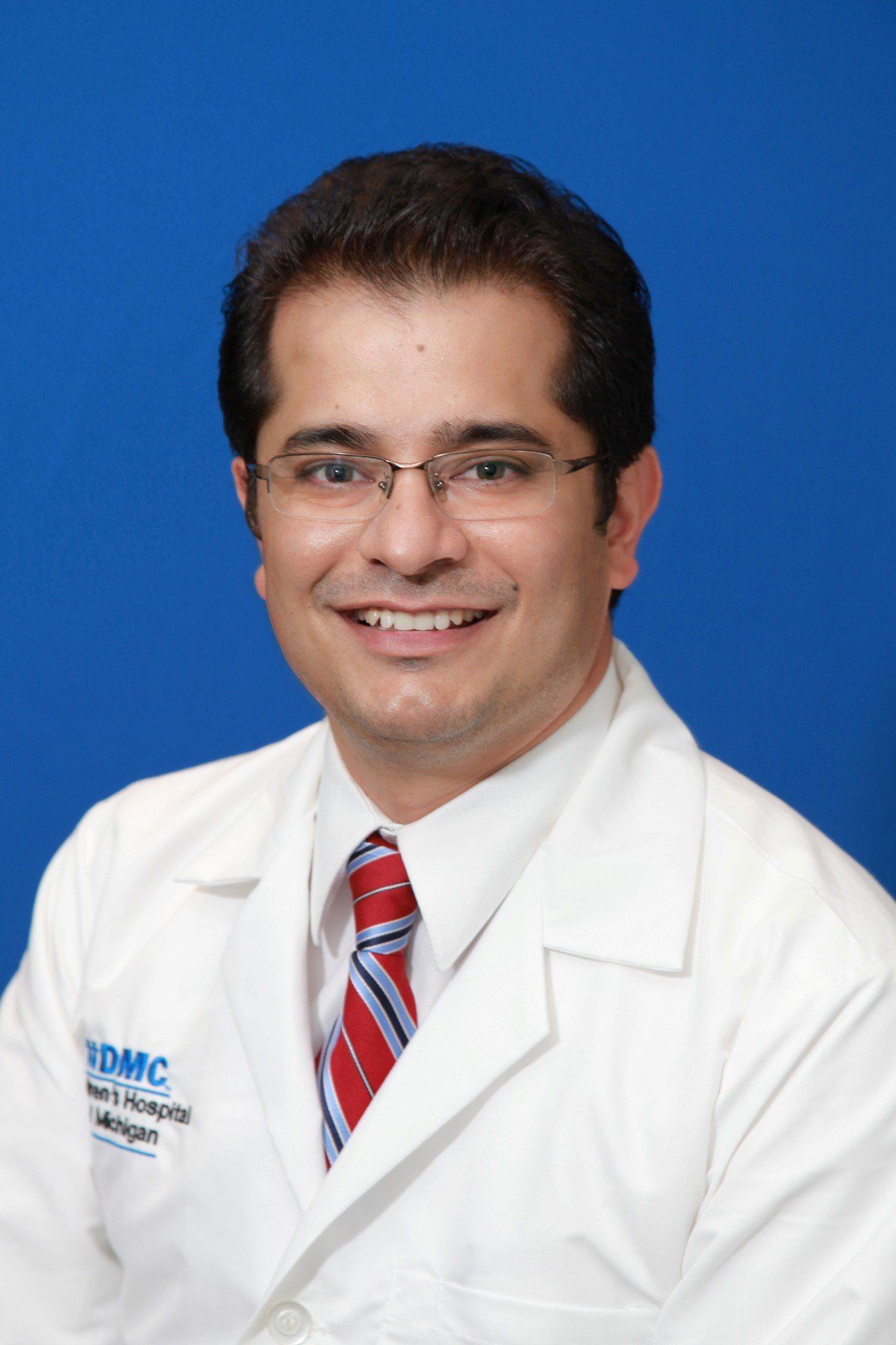 A man in a white lab coat and tie is smiling for the camera