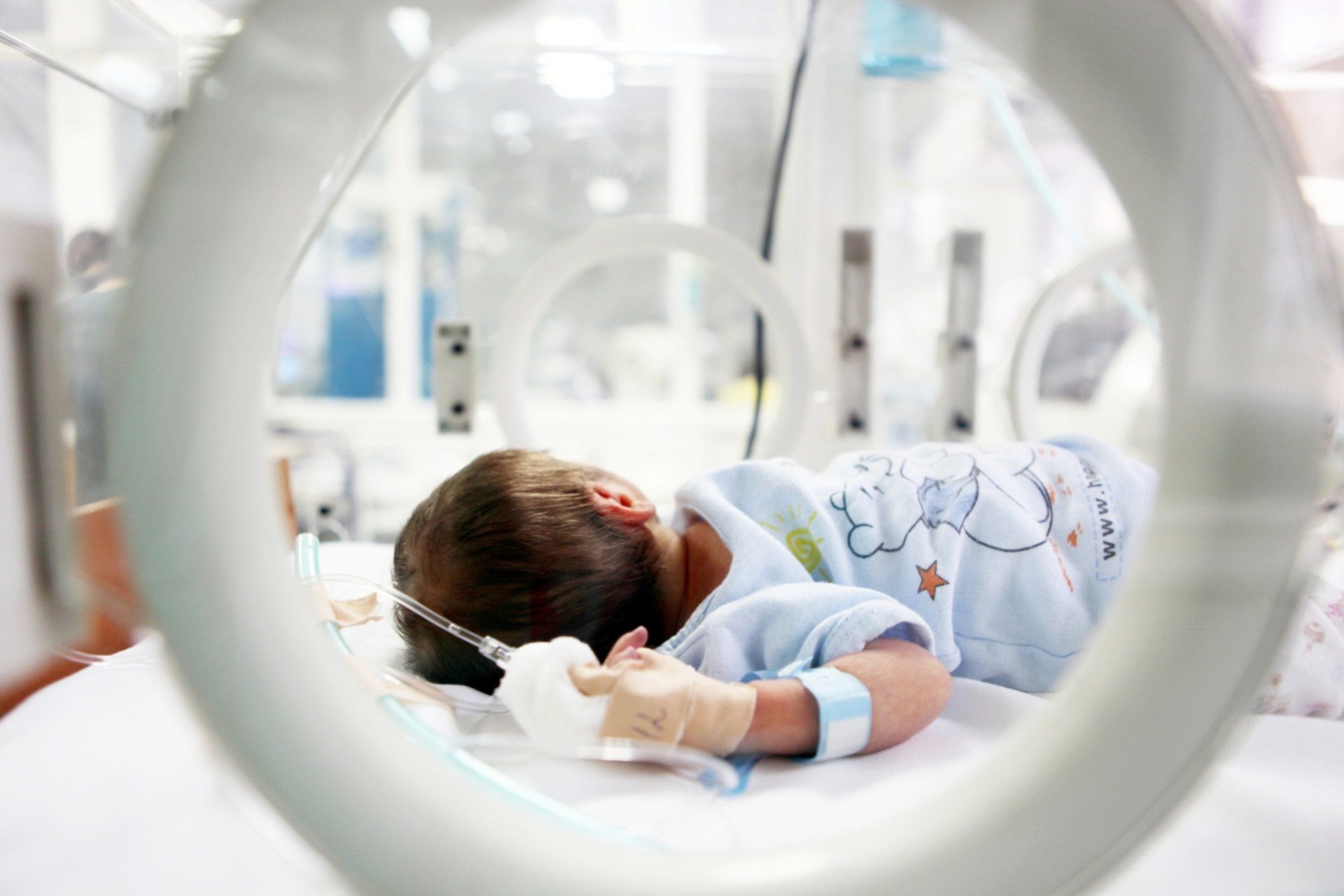 closeup of infant in NICU hospital bed through examination openings