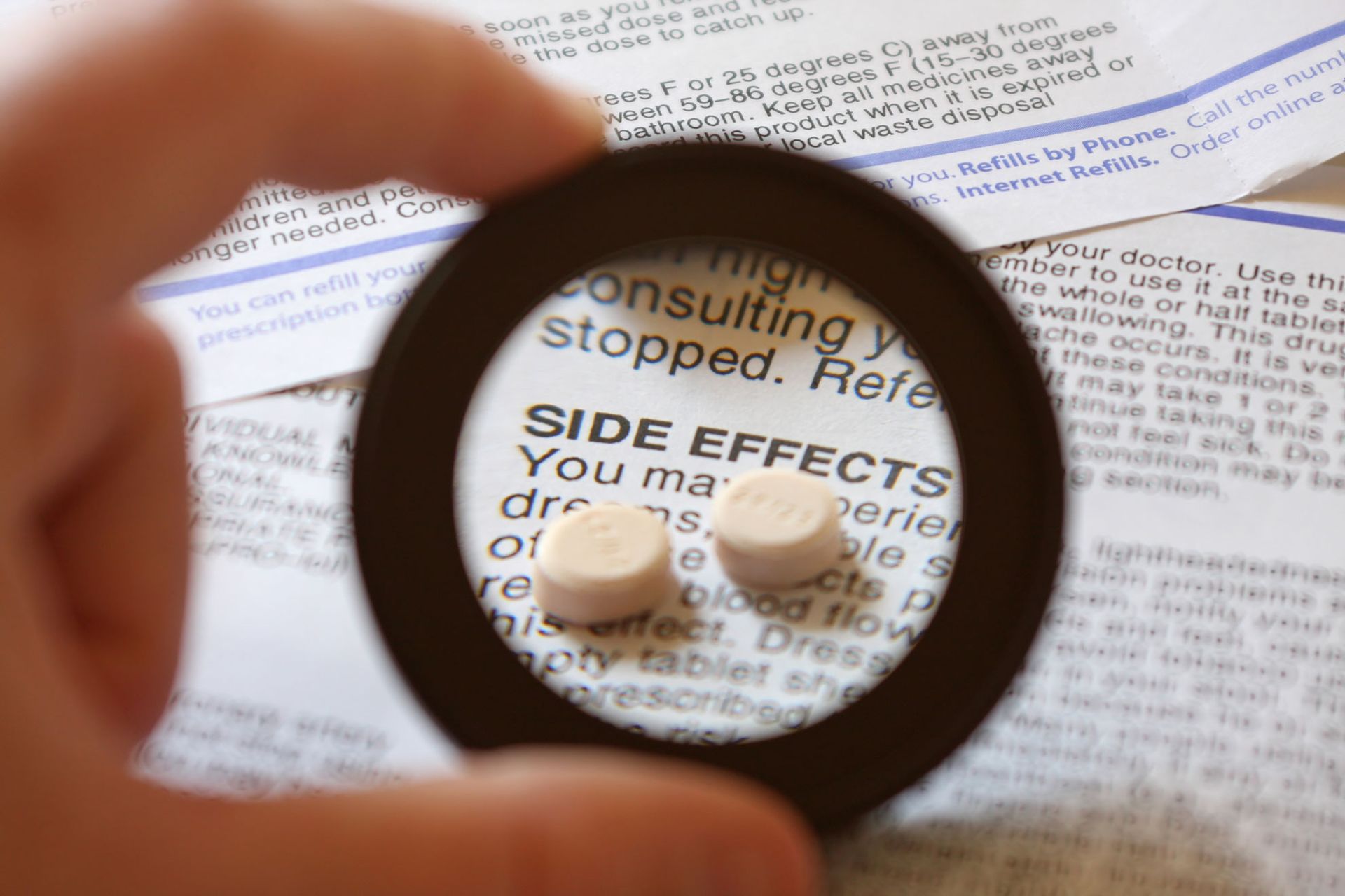 A person is holding a magnifying glass over a prescription for side effects