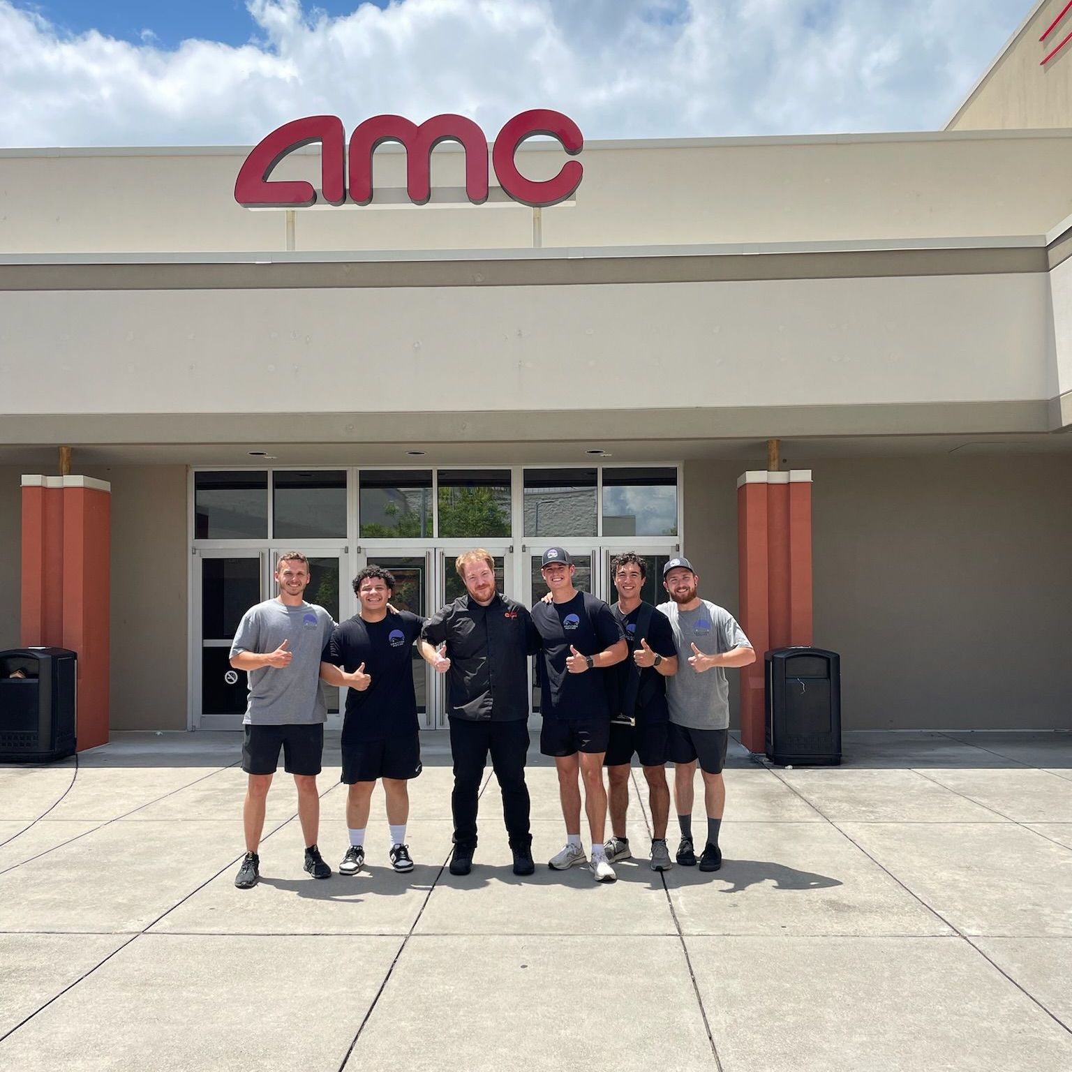 A group of men are posing for a picture in front of an amc building.