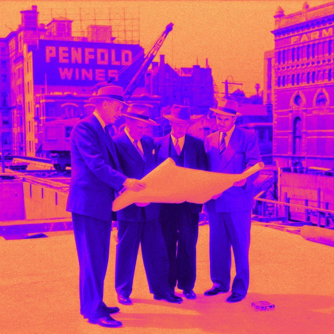 Four men in suits examining a large blueprint on a rooftop, with a 