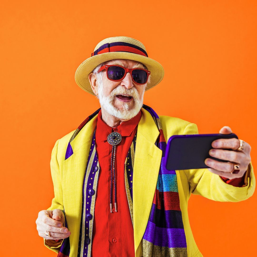 Man in bright clothing and hat taking a selfie against an orange background.