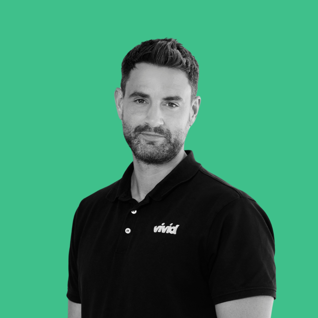 Man with dark hair and beard, wearing a black polo shirt, in front of a green backdrop.