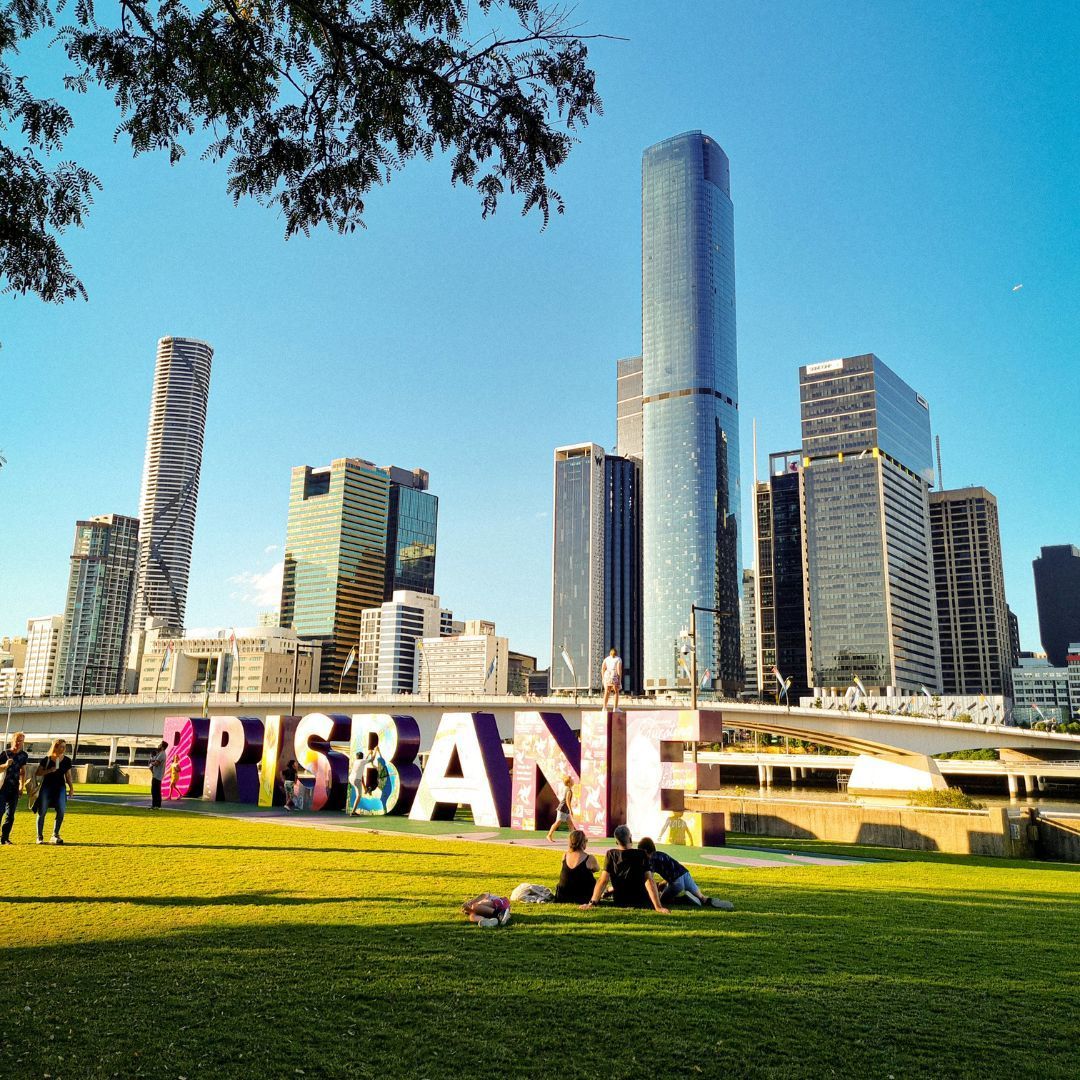 Brisbane riverfront skyline with colorful sign, green lawn, and clear blue sky