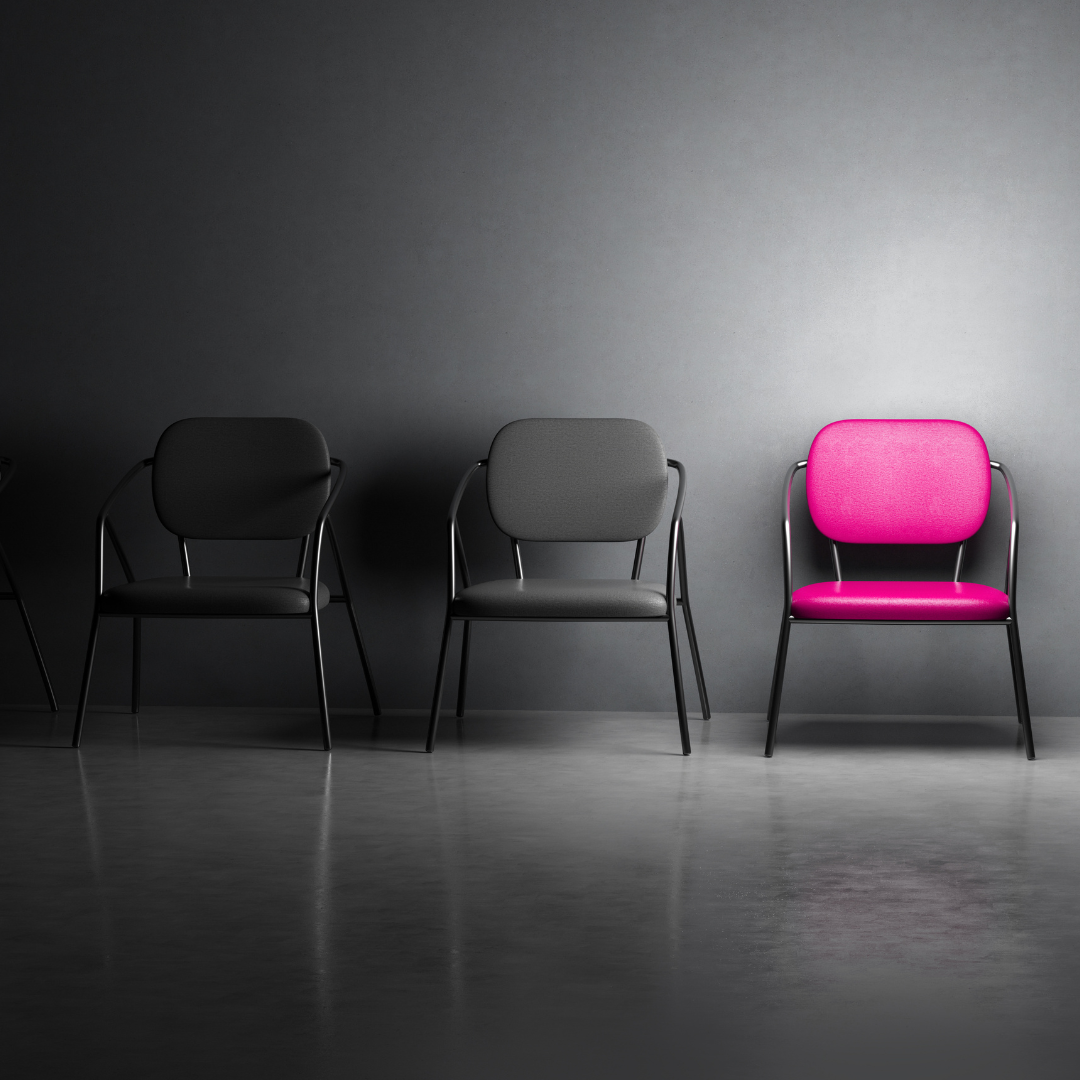 Three chairs on a dark stage, with one bright pink chair standing out