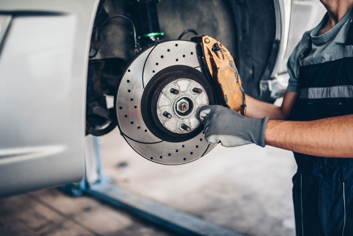 Mechanic replacing a brake rotor on a car in a garage.