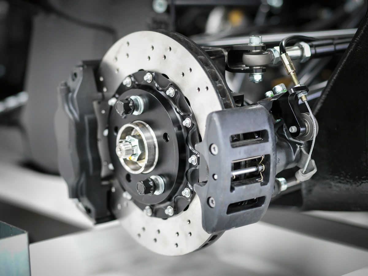 Car brake assembly, black caliper, silver rotor with holes, mounted on a vehicle chassis.