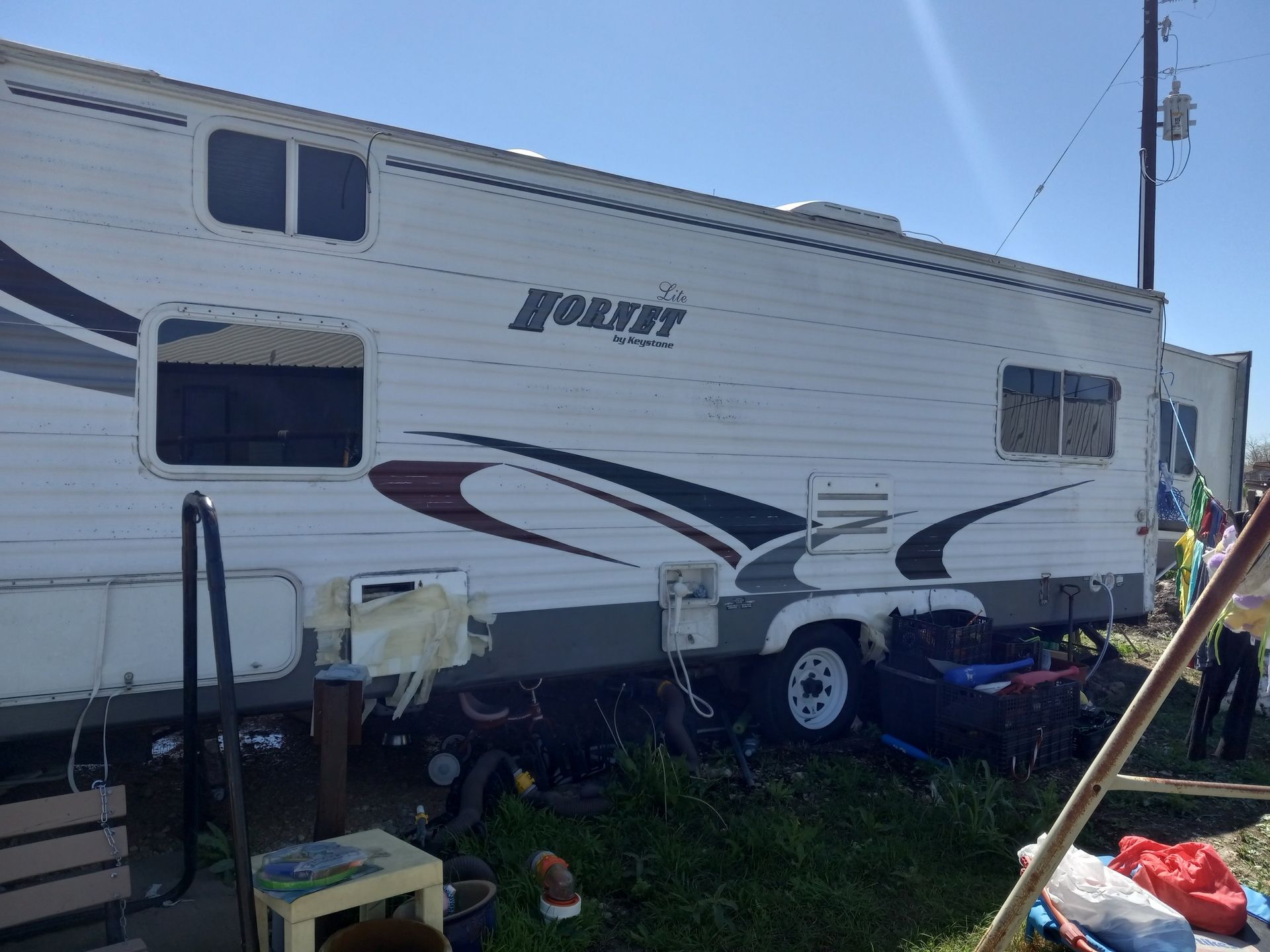 A white and grey Noble travel trailer parked outdoors on a sunny day, with various items scattered underneath.
