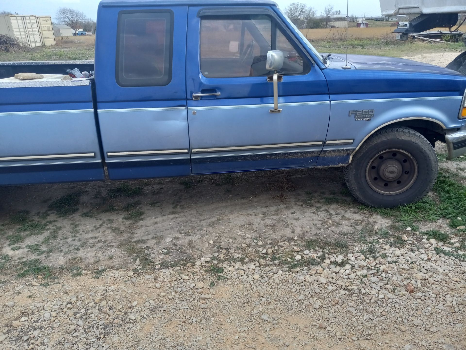 A two-tone blue Ford pickup truck parked on a gravel surface.