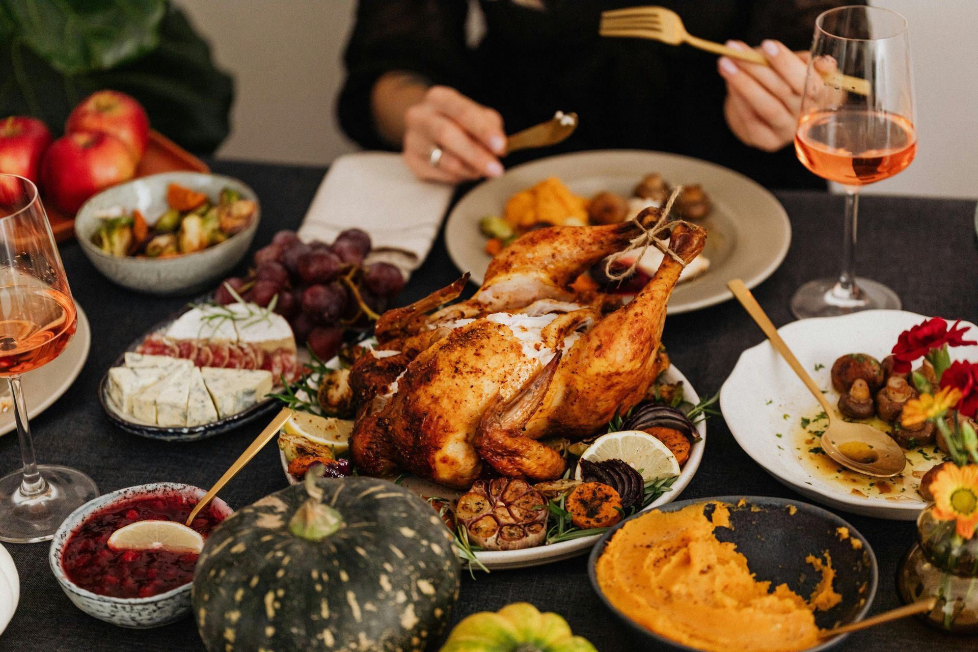Thanksgiving feast on a table: Roasted turkey, side dishes, wine glasses, and a person eating.