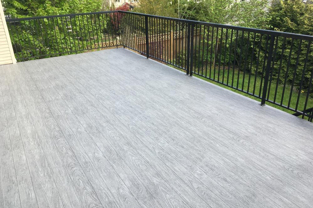 Une terrasse grise avec une rampe noire et des arbres en arrière-plan.