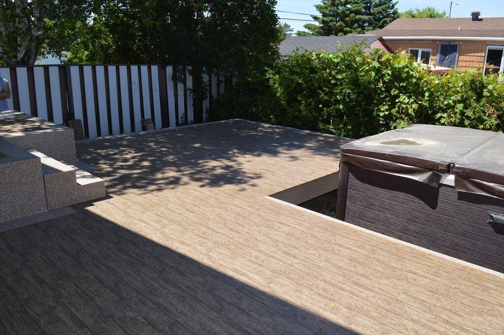 Une terrasse avec membrane de pvc avec un bain à remous et une clôture en arrière-plan