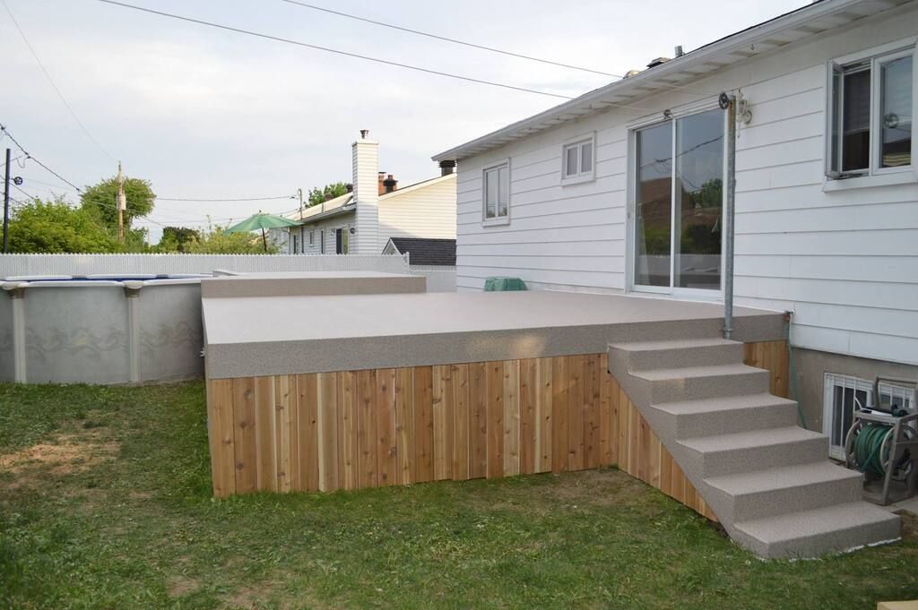 Une maison avec une terrasse en bois couverte d'une membrane de pvc et des escaliers devant elle