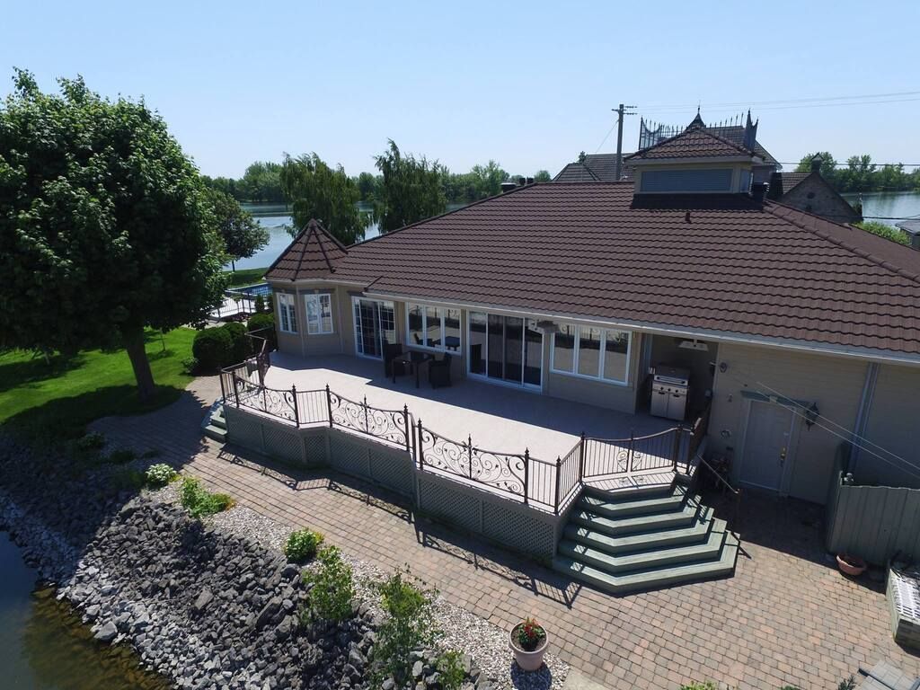 Une vue aérienne d'une grande maison avec une grande terrasse avec membrane de pvc à côté d'un plan d'eau