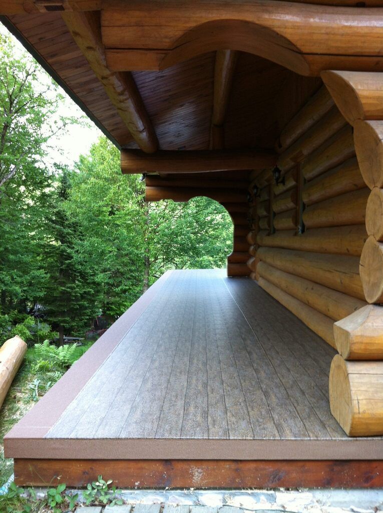 Une maison en rondins avec un porche couvert de pvc entouré d'arbres