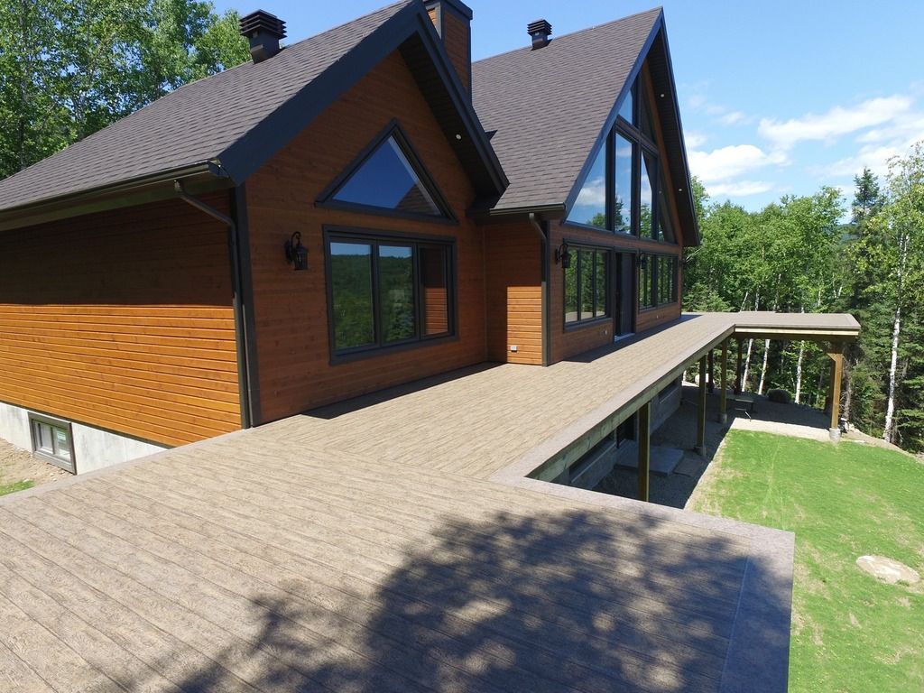 Une vue aérienne d'une grande maison avec une grande terrasse avec membrane de pvc entourée d'arbres.