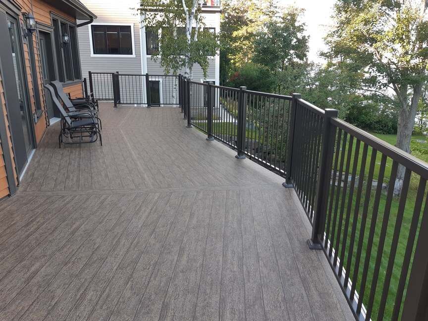 Une grande terrasse recouverte de membrane de pvc avec une balustrade noire et des chaises dessus.