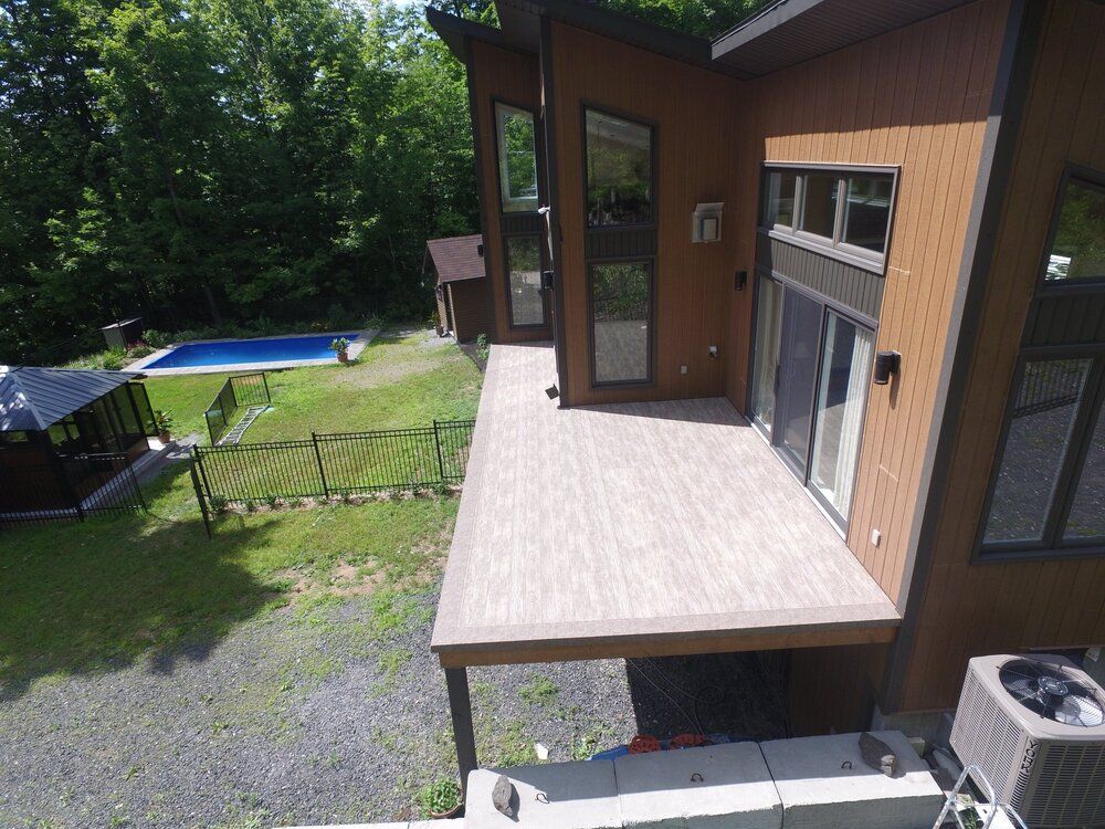 Une vue aérienne d'une maison avec une grande terrasse  en membrane de pvc et une piscine dans l'arrière-cour.