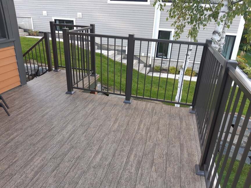 Une terrasse en membrane de pvc avec une balustrade en métal et des escaliers menant à une maison.